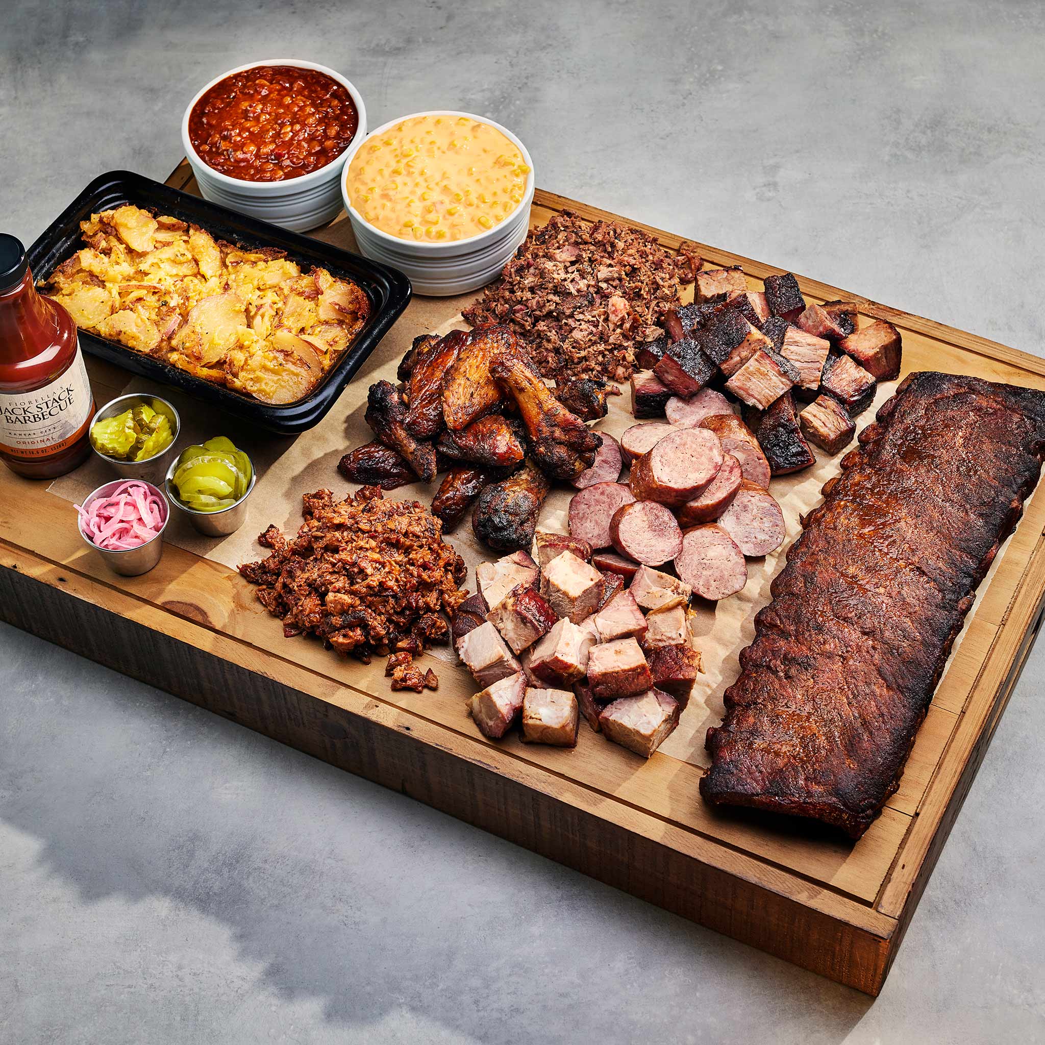 Assorted barbecue meats and sides on a wooden board with a gray background