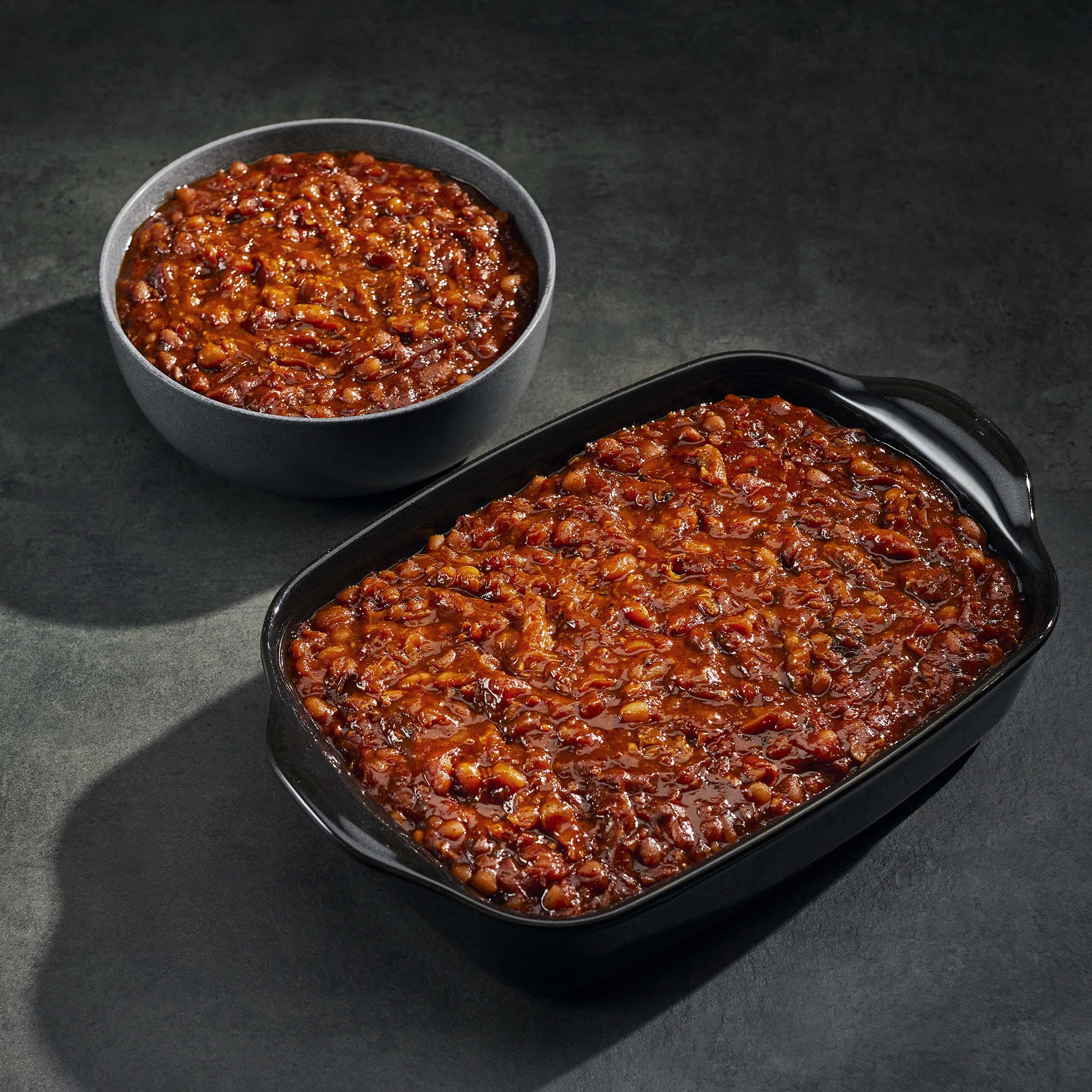 Baked beans in a bowl and a dish on a dark surface