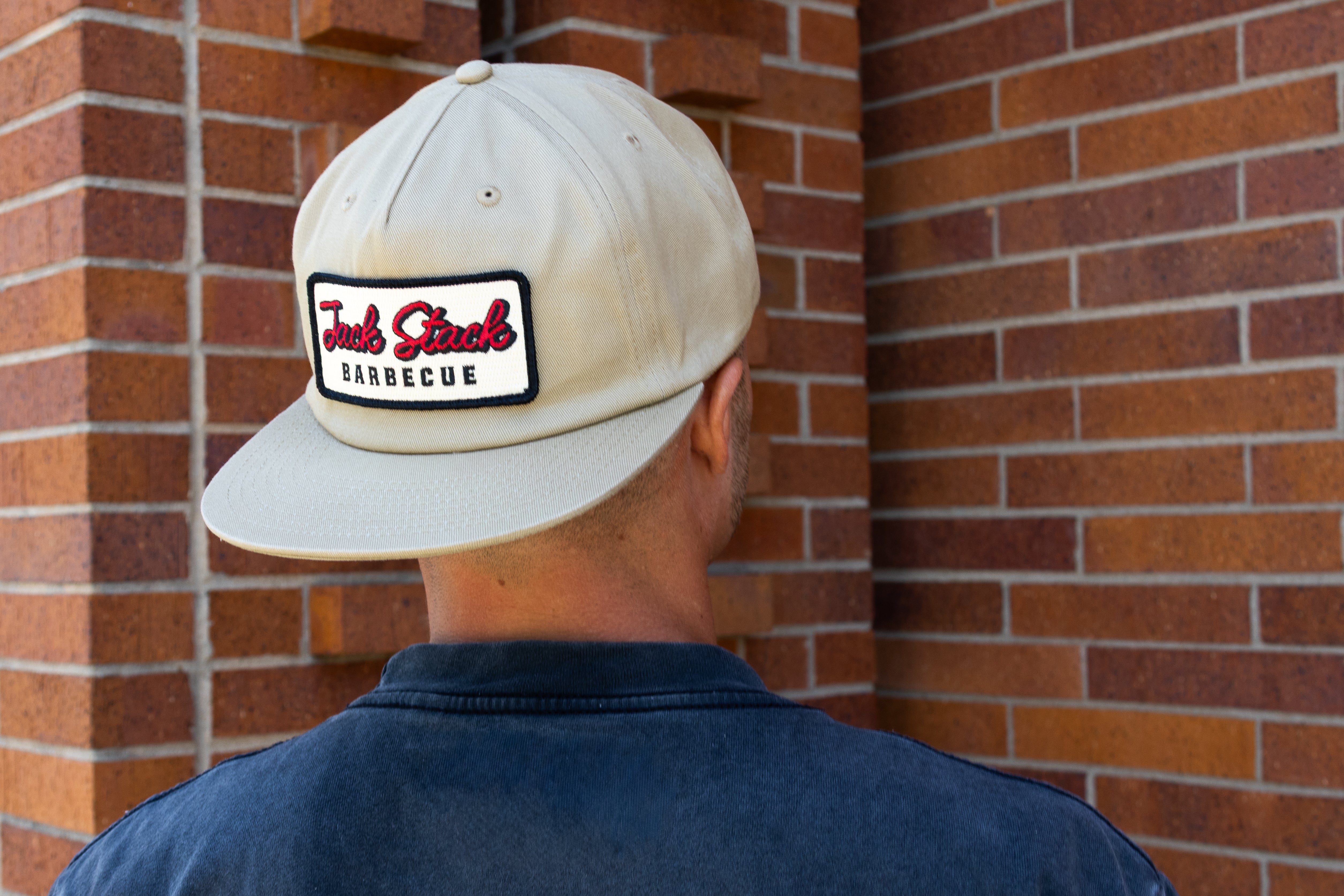Person wearing a cap with 'Jack Stack Barbecue' logo against a brick wall