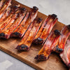 Grilled ribs on a wooden cutting board with a neutral background