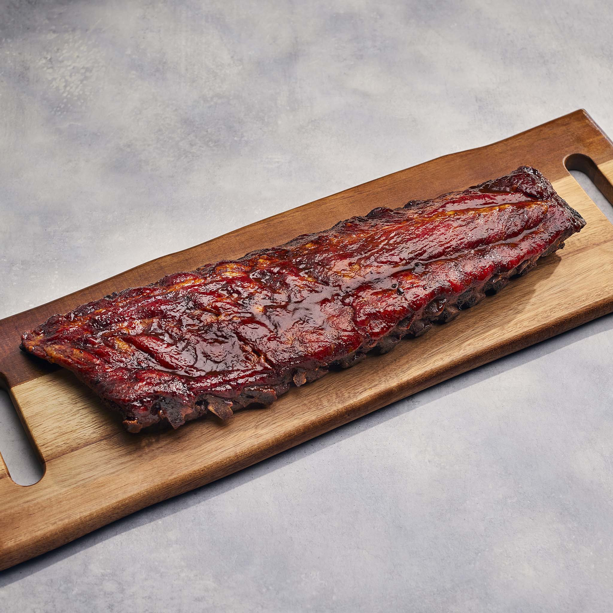 Barbecue ribs on a wooden cutting board with a gray background