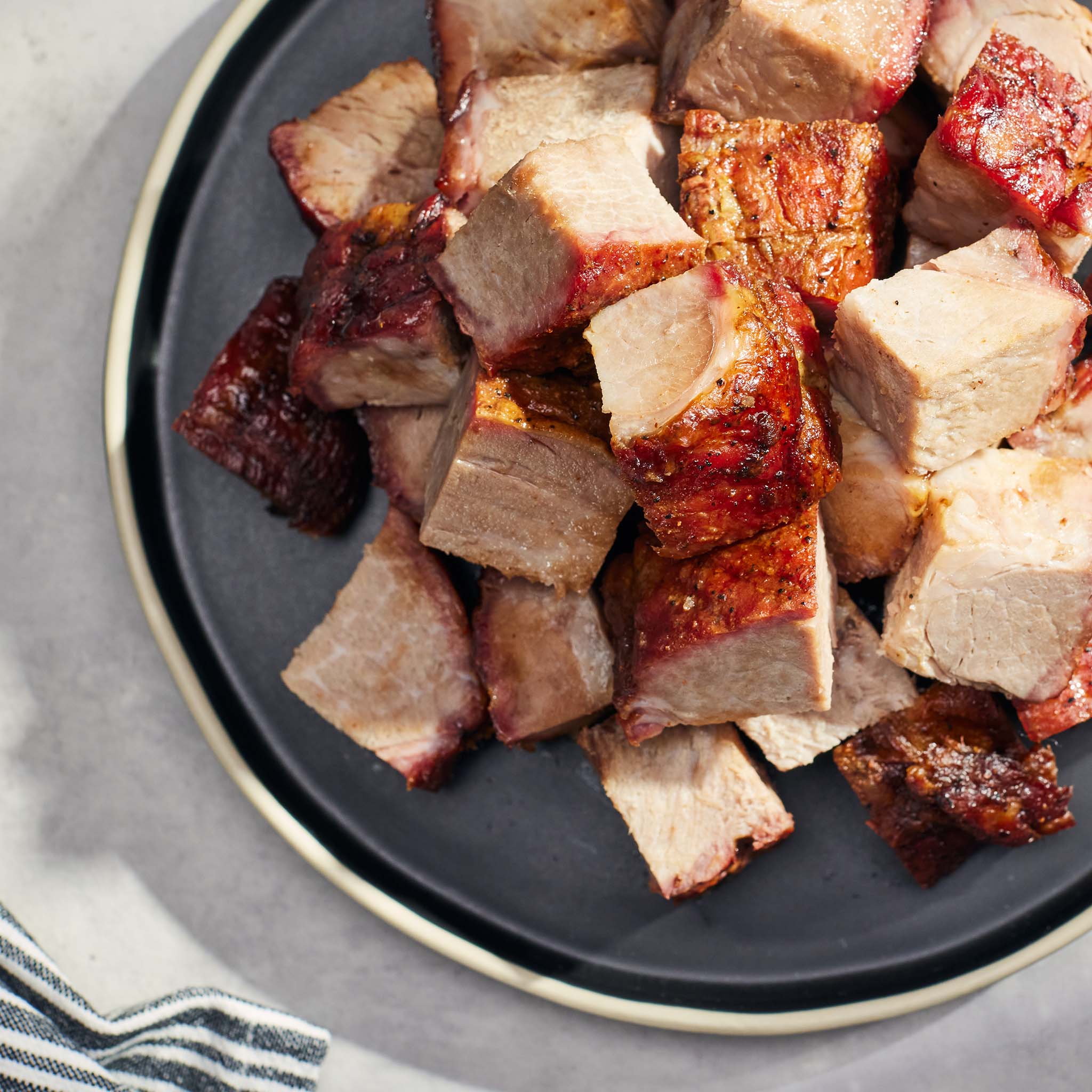 Pork burnt ends on a dark plate with a striped cloth in the background