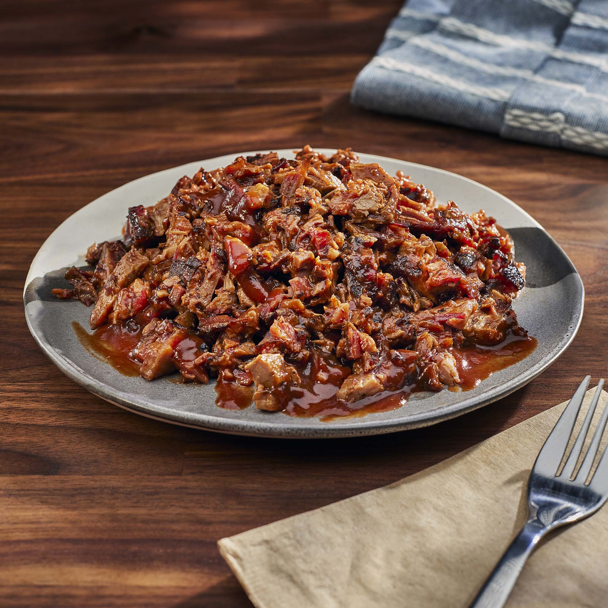 Plated dish of pulled pork with sauce on a wooden table with a fork and napkin.