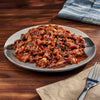 Plated dish of pulled pork with sauce on a wooden table with a fork and napkin.