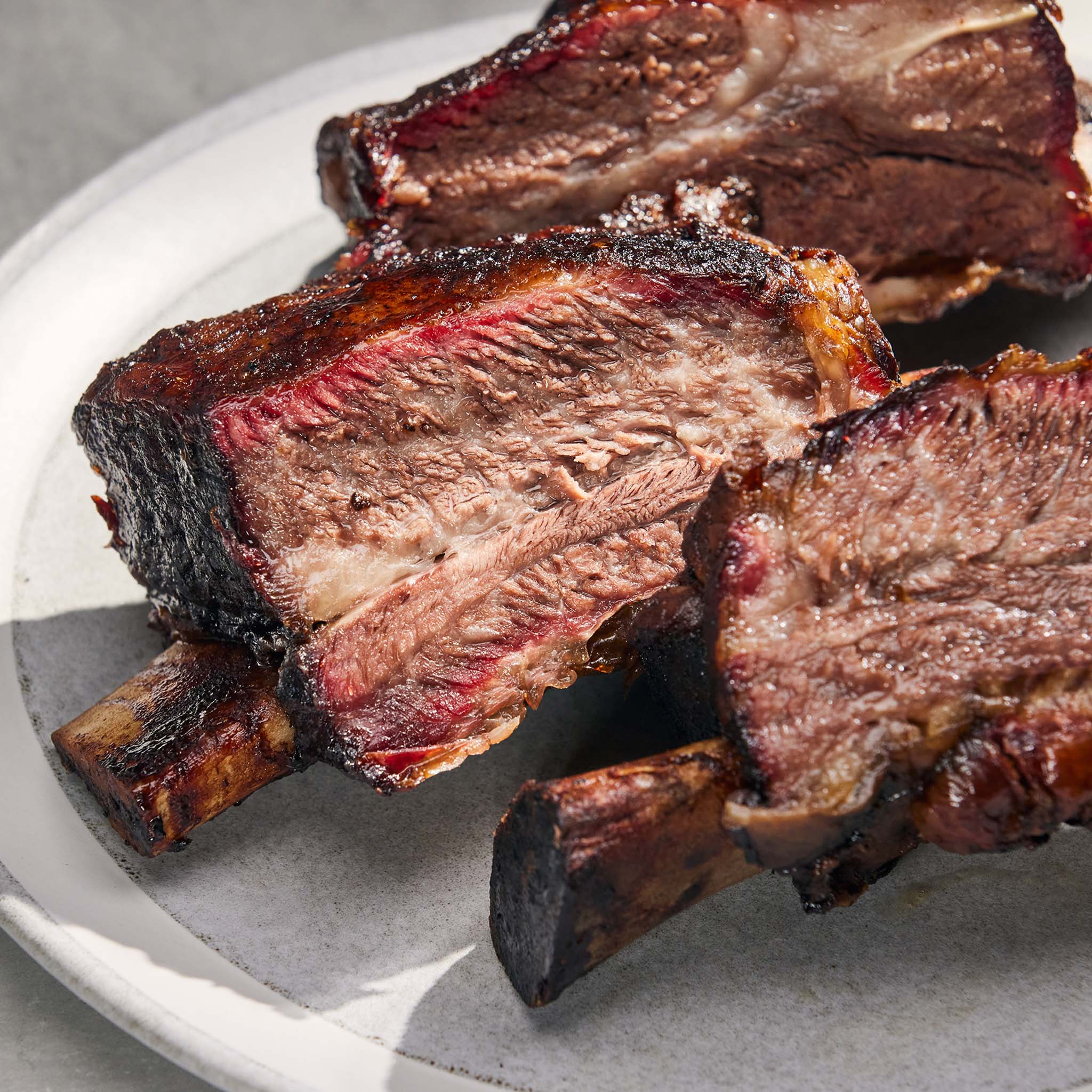 Close-up of cooked beef ribs on a white plate with a gray background