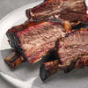 Close-up of cooked beef ribs on a white plate with a gray background