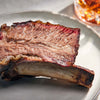 Close-up of a rib on a plate with a glass of amber liquid in the background