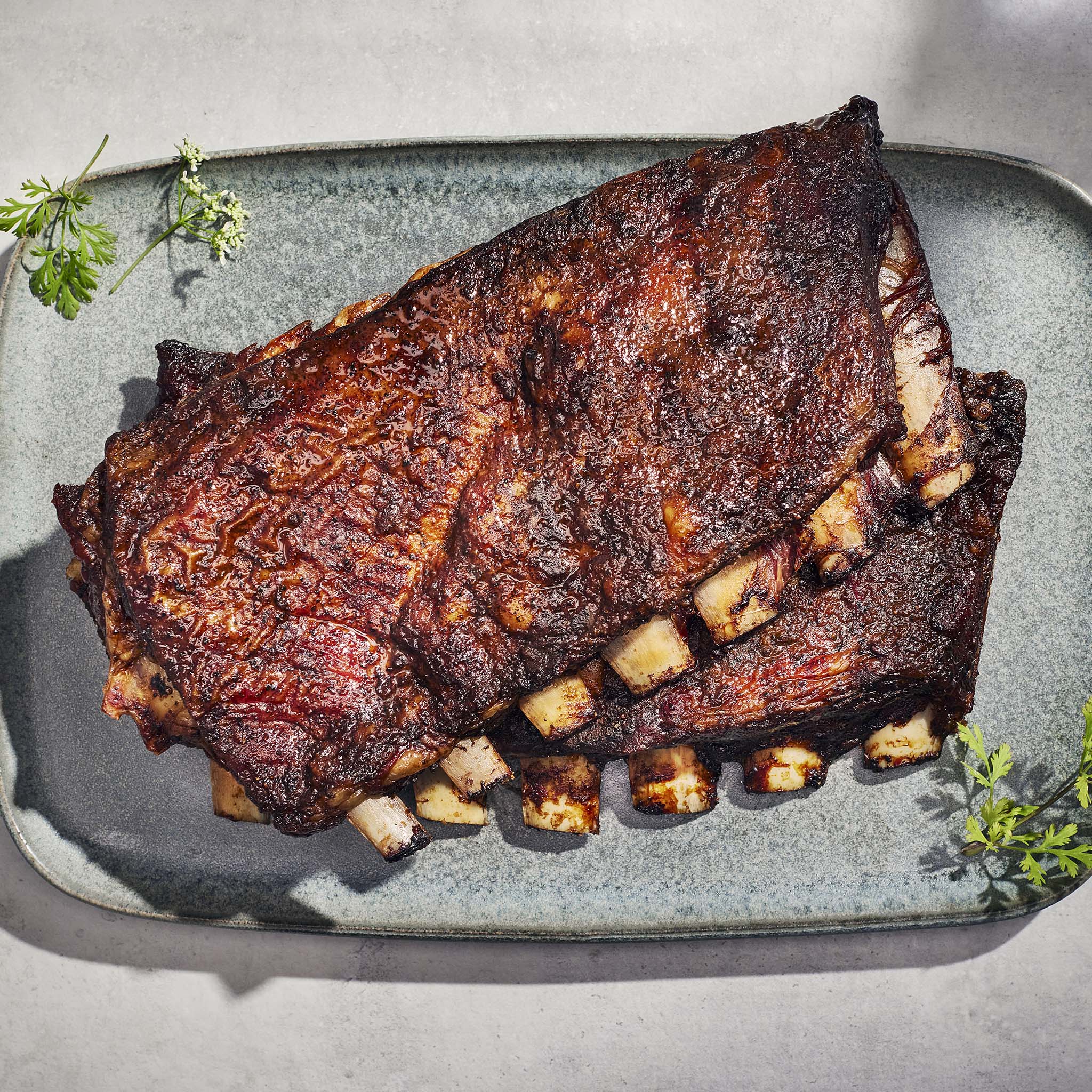 Barbecue ribs on a gray rectangular plate with green herbs.