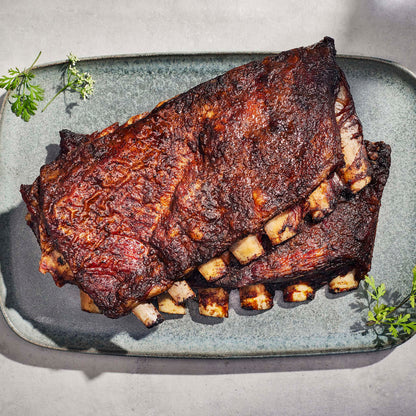 Barbecue ribs on a gray rectangular plate with green herbs.