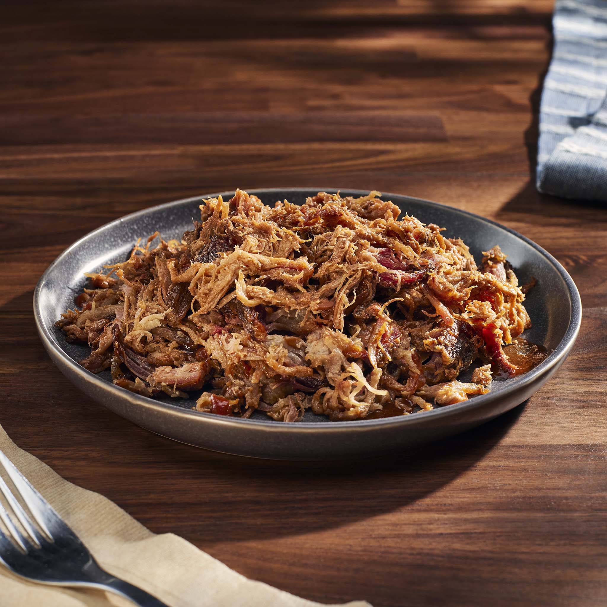 Plated dish of pulled pork on a wooden table with a fork and napkin.
