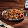 Plated dish of pulled pork on a wooden table with a fork and napkin.