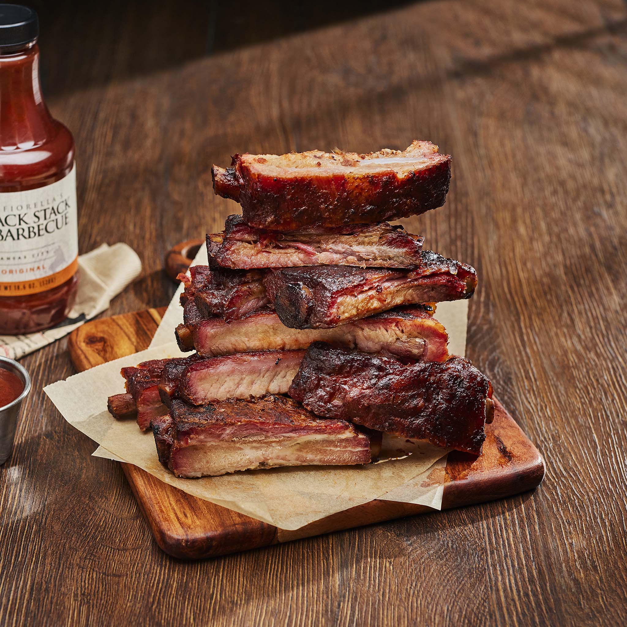 Stack of ribs on a wooden cutting board with a bottle of barbecue sauce in the background.