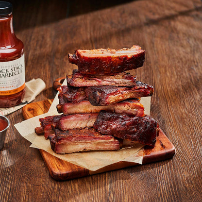 Stack of ribs on a wooden cutting board with a bottle of barbecue sauce in the background.