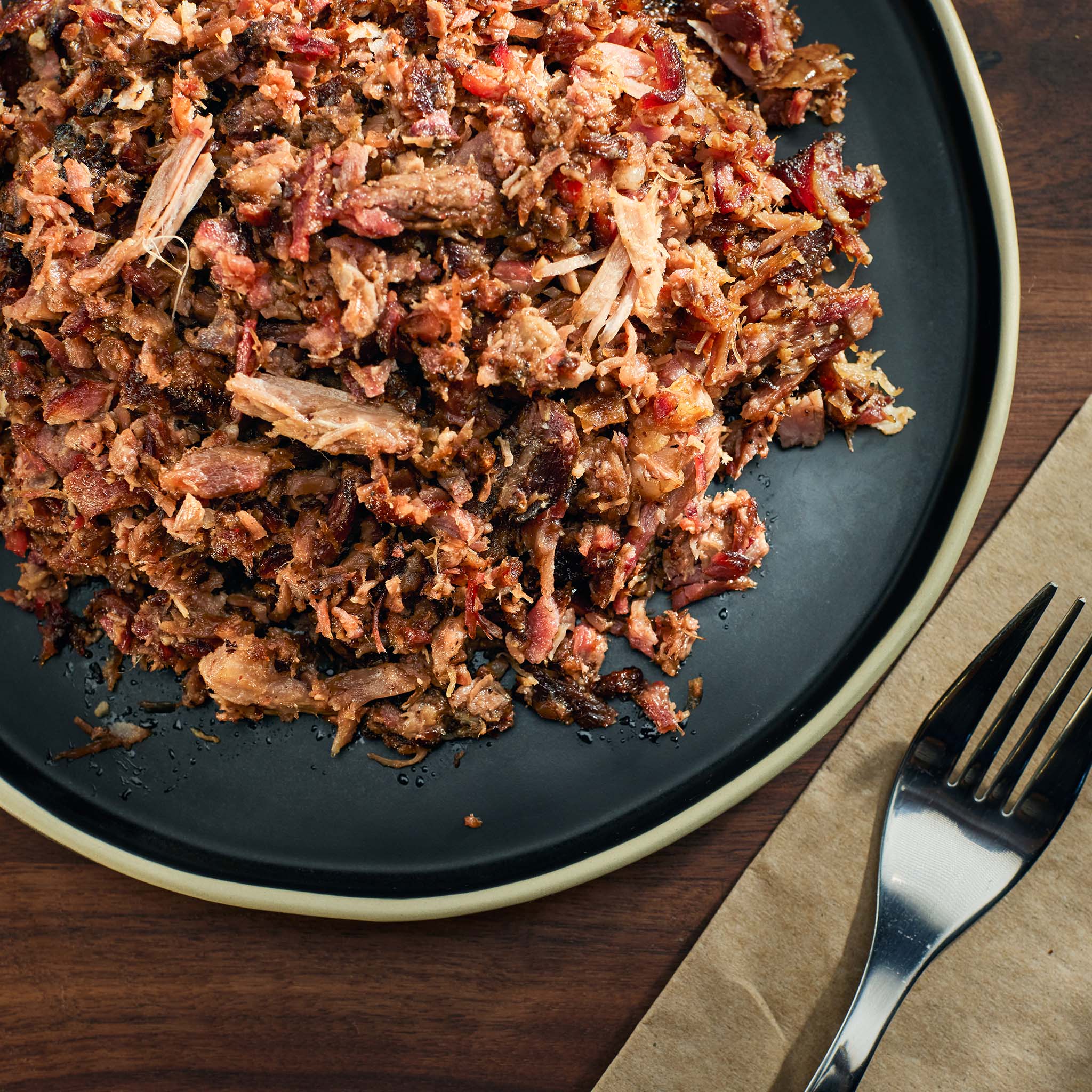 Shredded meat on a dark plate with a fork and napkin on a wooden surface