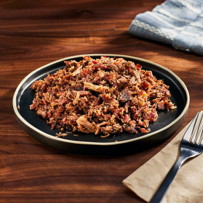 Plated dish of pulled pork on a wooden table with a napkin and fork.