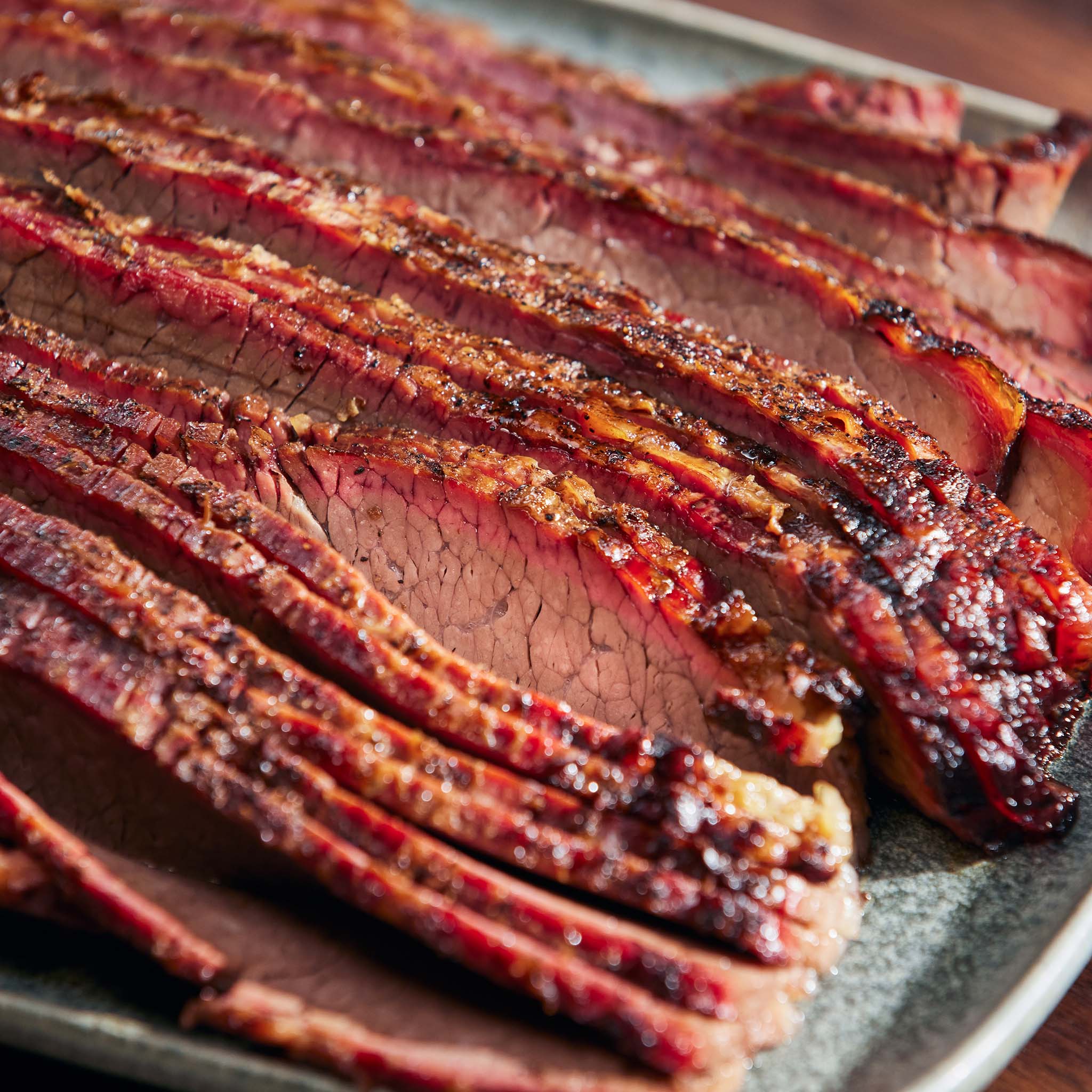 Sliced smoked meat on a plate with a wooden background