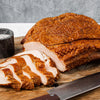 Sliced roasted pork on a wooden cutting board with a knife and salt grinder.