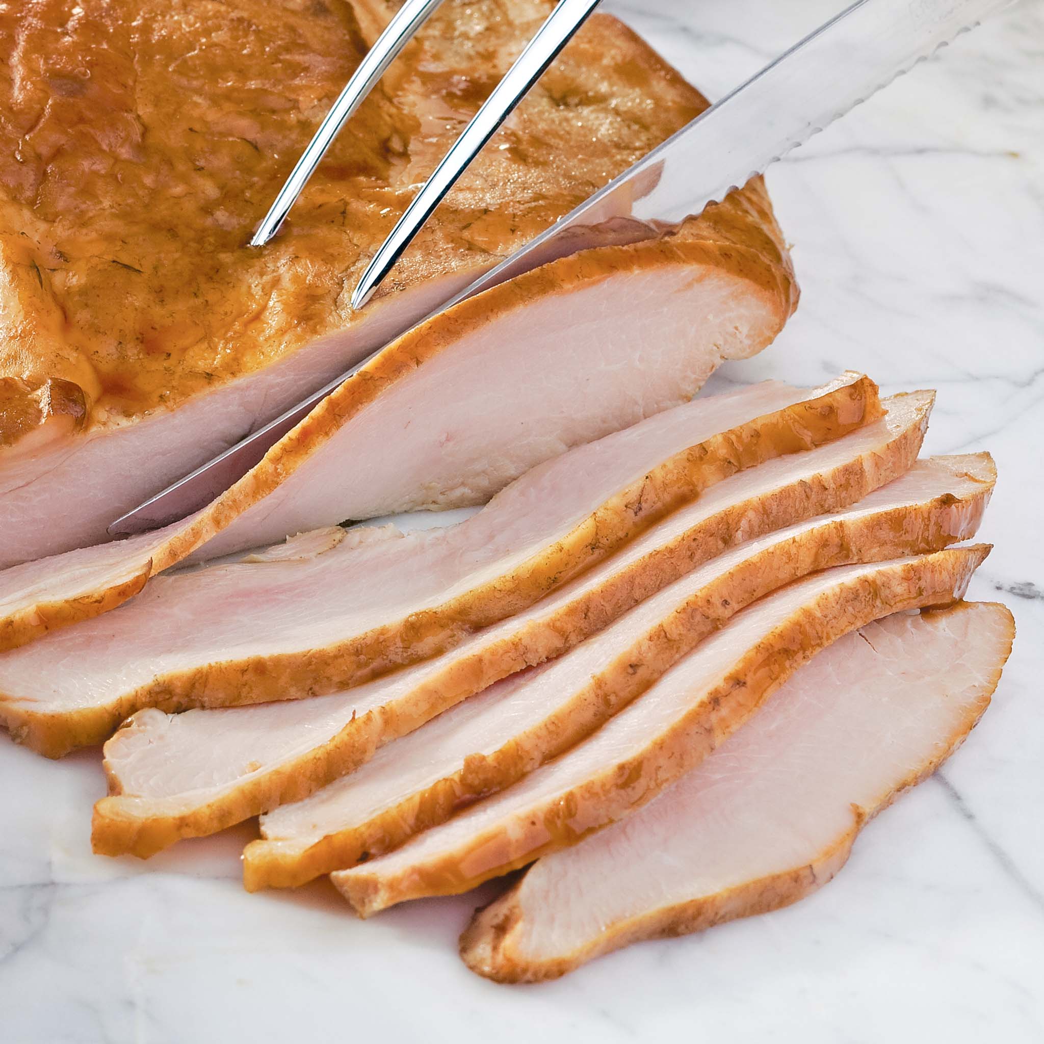 Sliced turkey with a knife and fork on a marble surface
