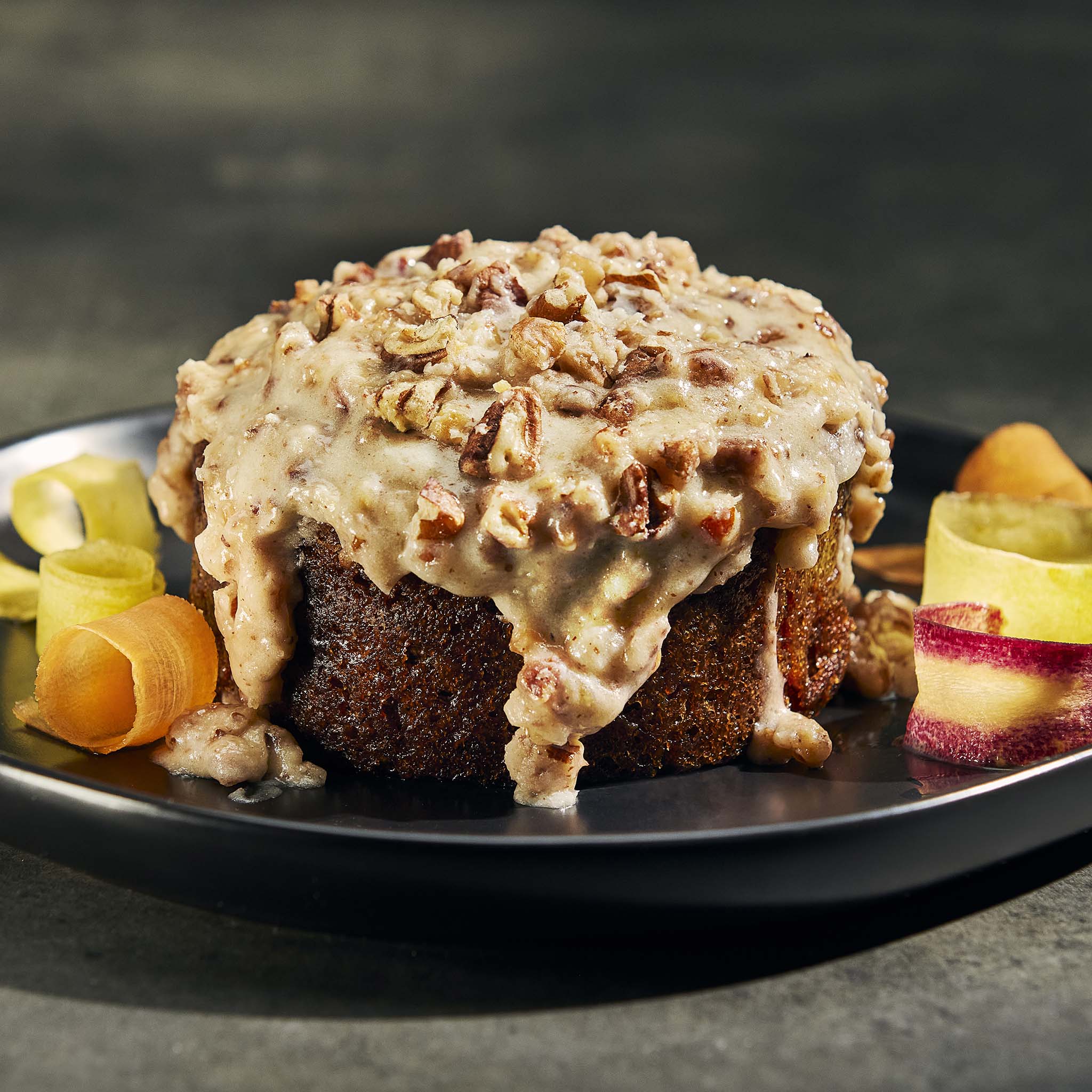 Carrot cake with creamy topping and pecans on a black plate