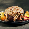 Carrot cake with creamy topping and pecans on a black plate