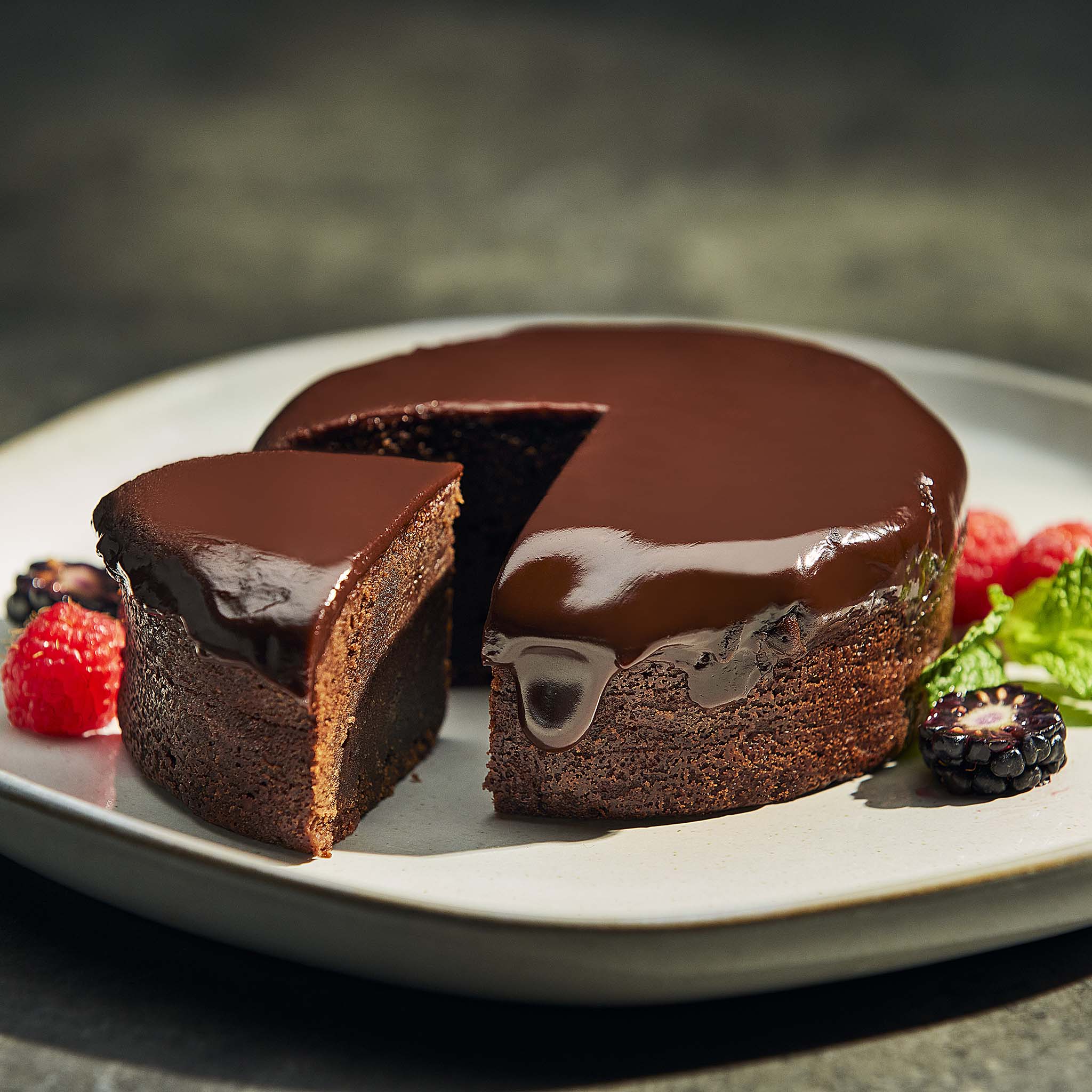 Triple chocolate brownie with a slice cut out on a plate with berries