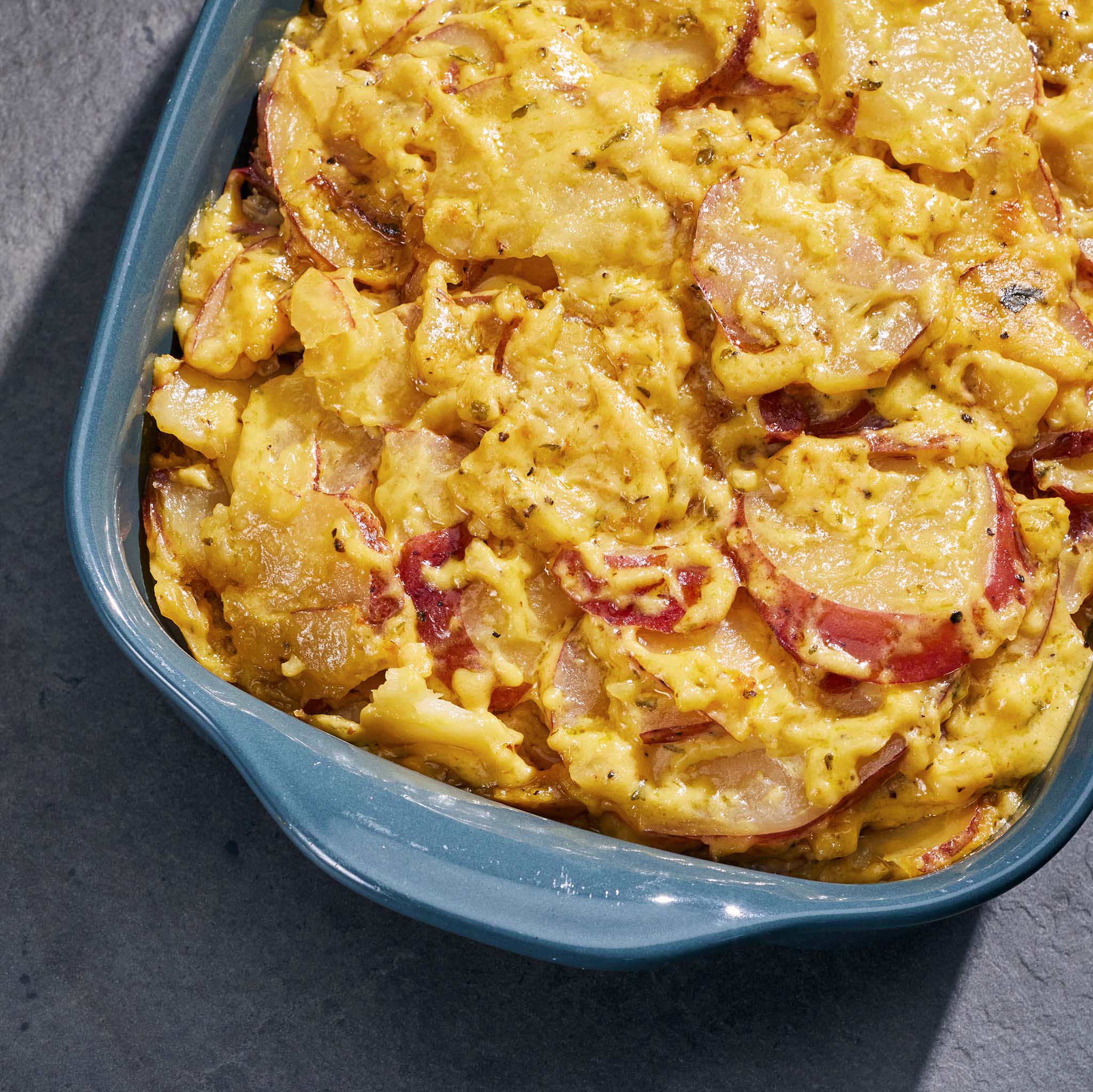 Cheesy potato bake in a blue baking dish on a dark surface