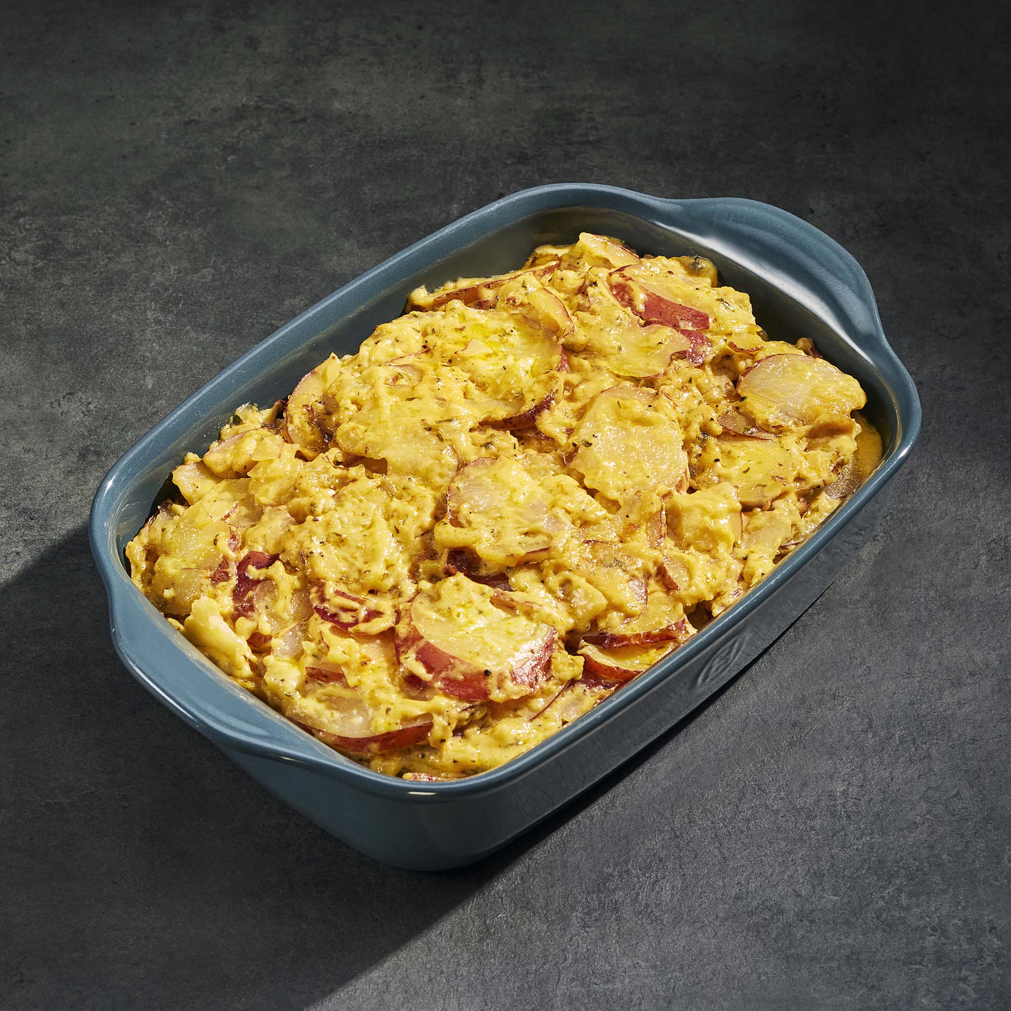 Cheesy potato bake in a blue container on a dark background