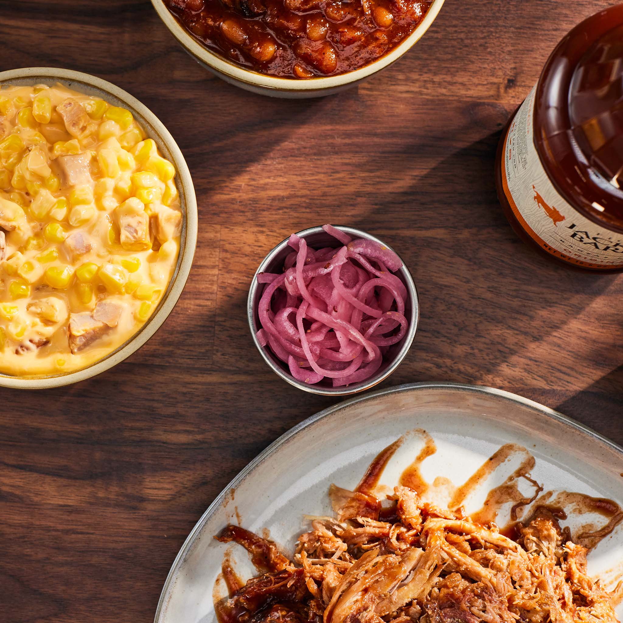 Assorted food items including macaroni and cheese, pulled pork, and pickled onions on a wooden table.