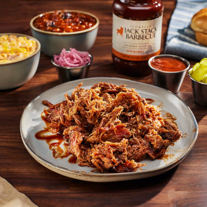 Plated pulled pork with Jack Stack Barbecue sauce on a wooden table with sides and a bottle of sauce.