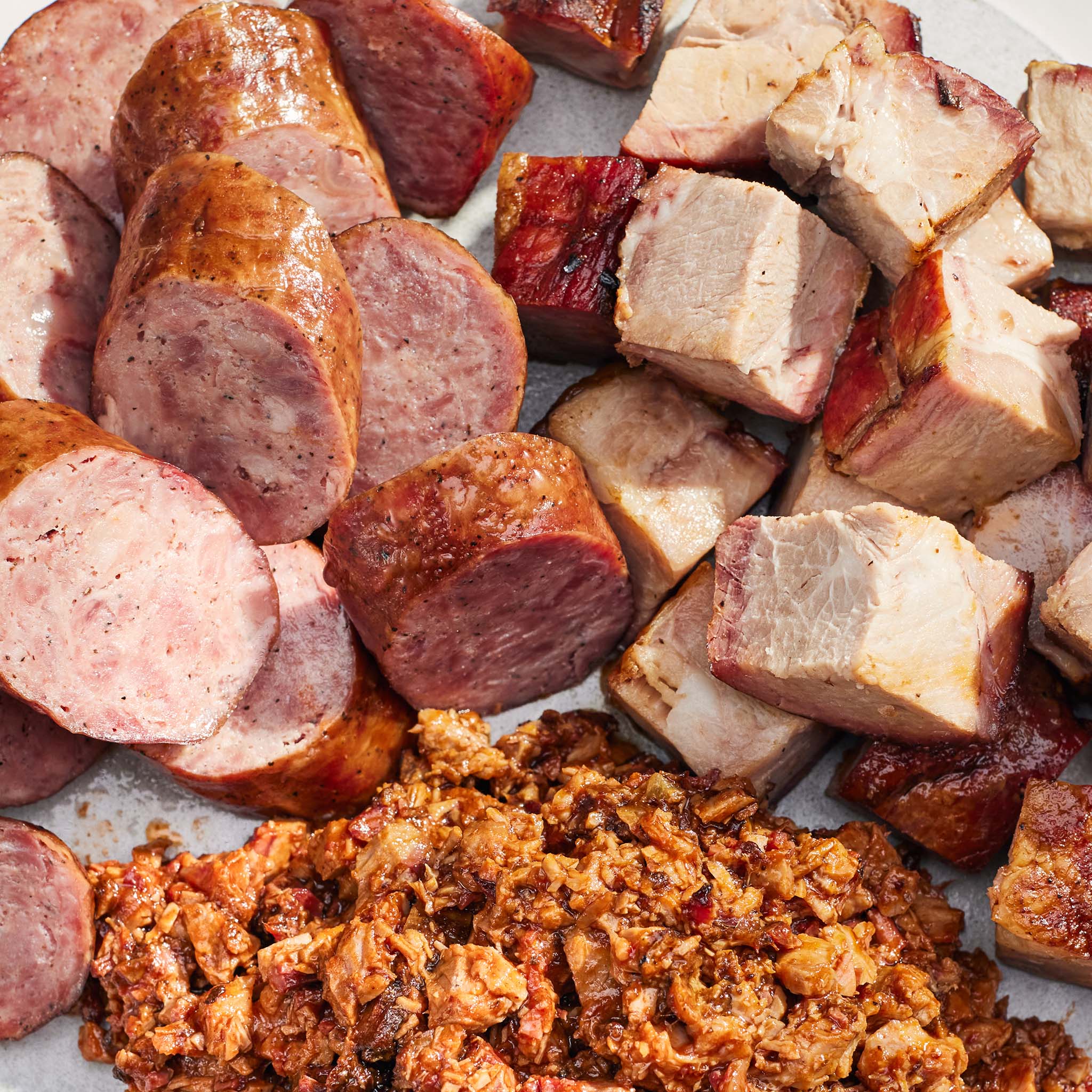 Assorted cuts of cured meats including sausages, bacon, and chopped ham on a white surface.