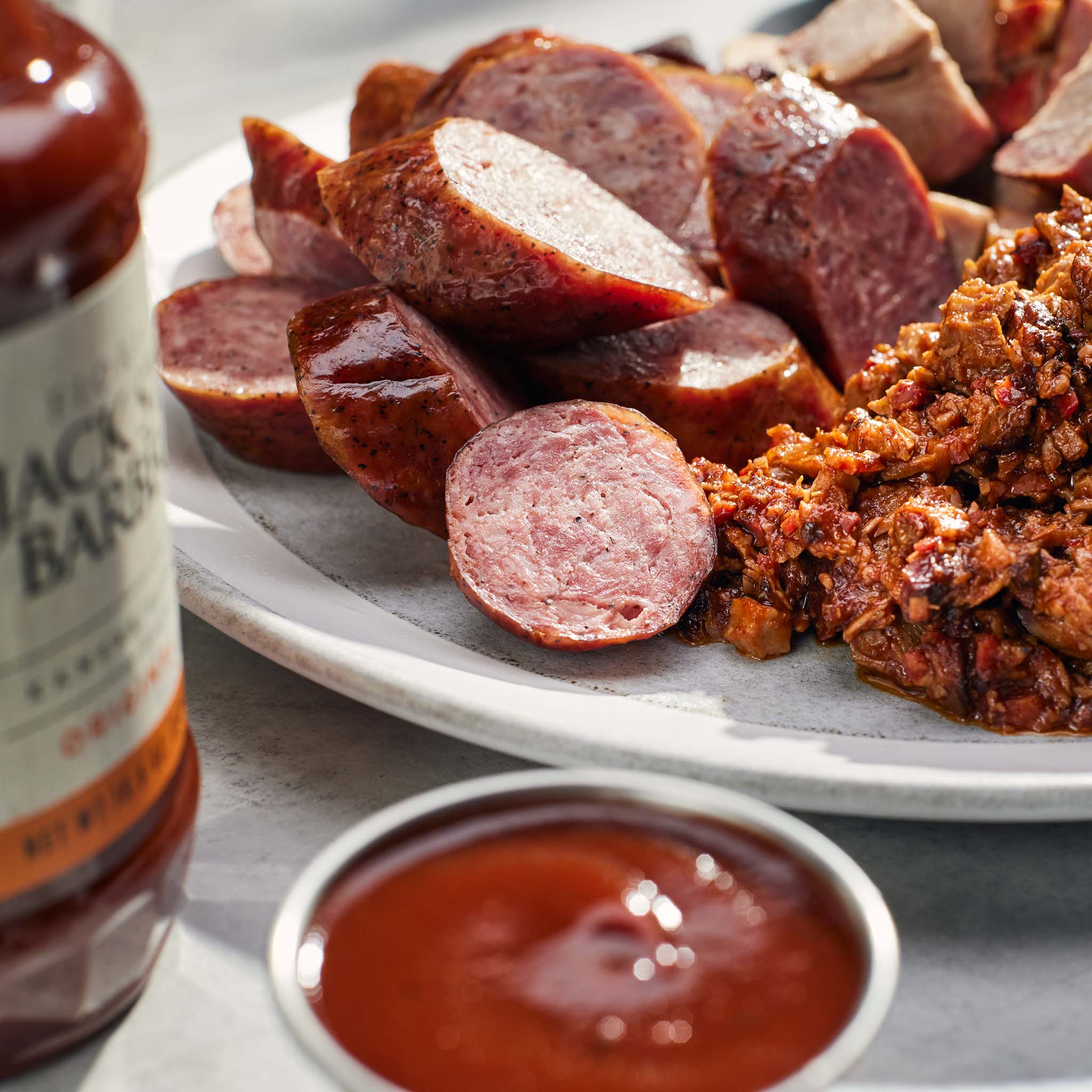 Plated sliced sausages with a side of chopped beef brisket and a bottle of Jack Stack barbecue sauce.