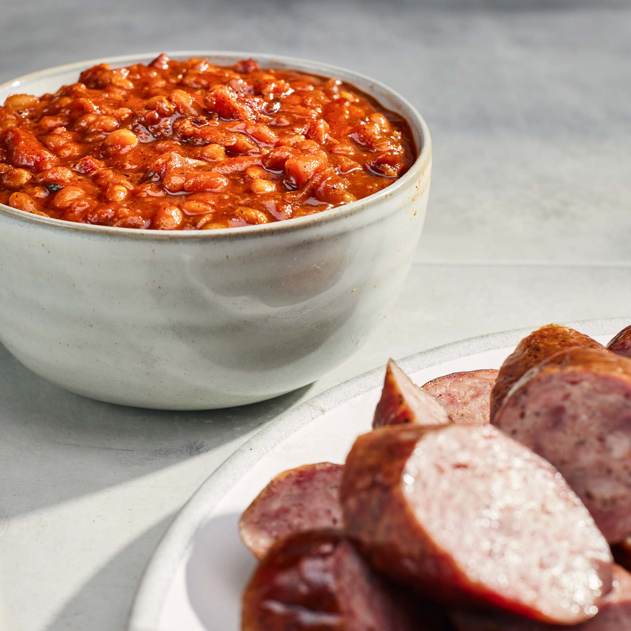 Bowl of baked beans with sliced sausages on a plate