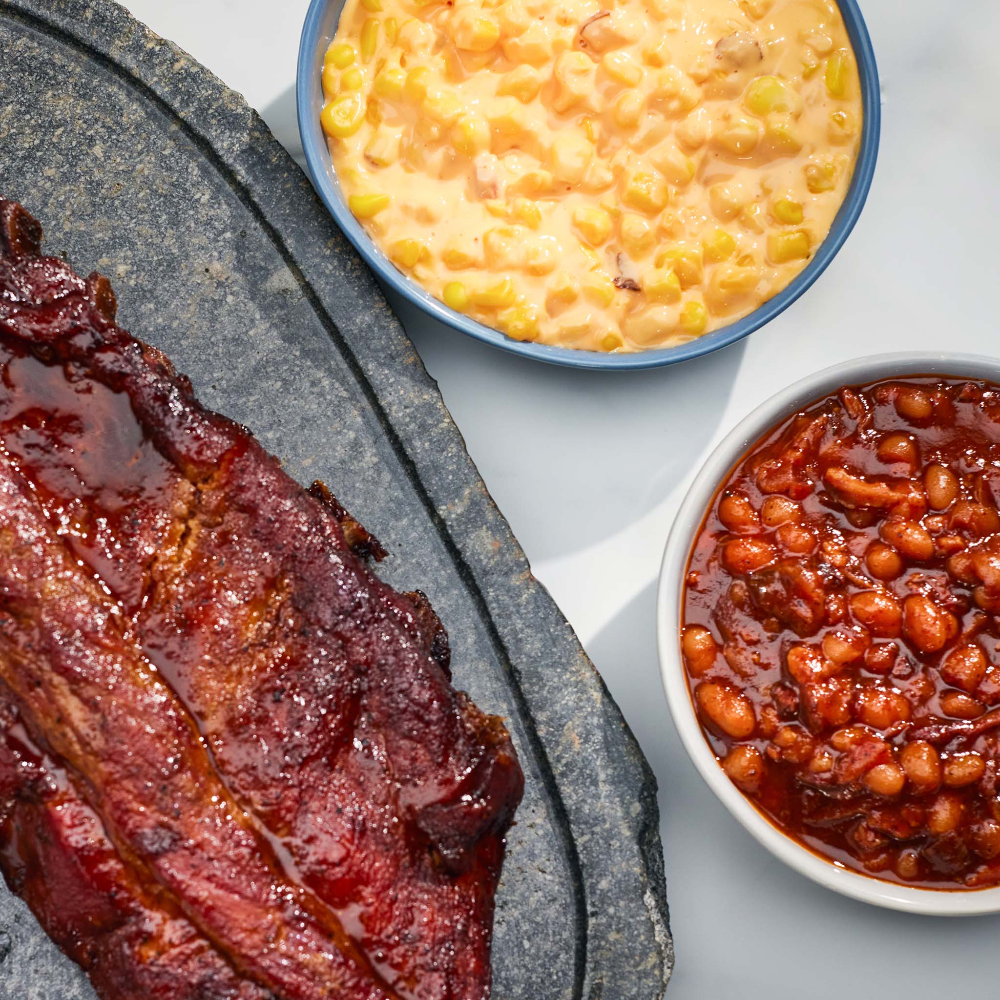 Bbq ribs with a side of corn and beans on a stone platter.