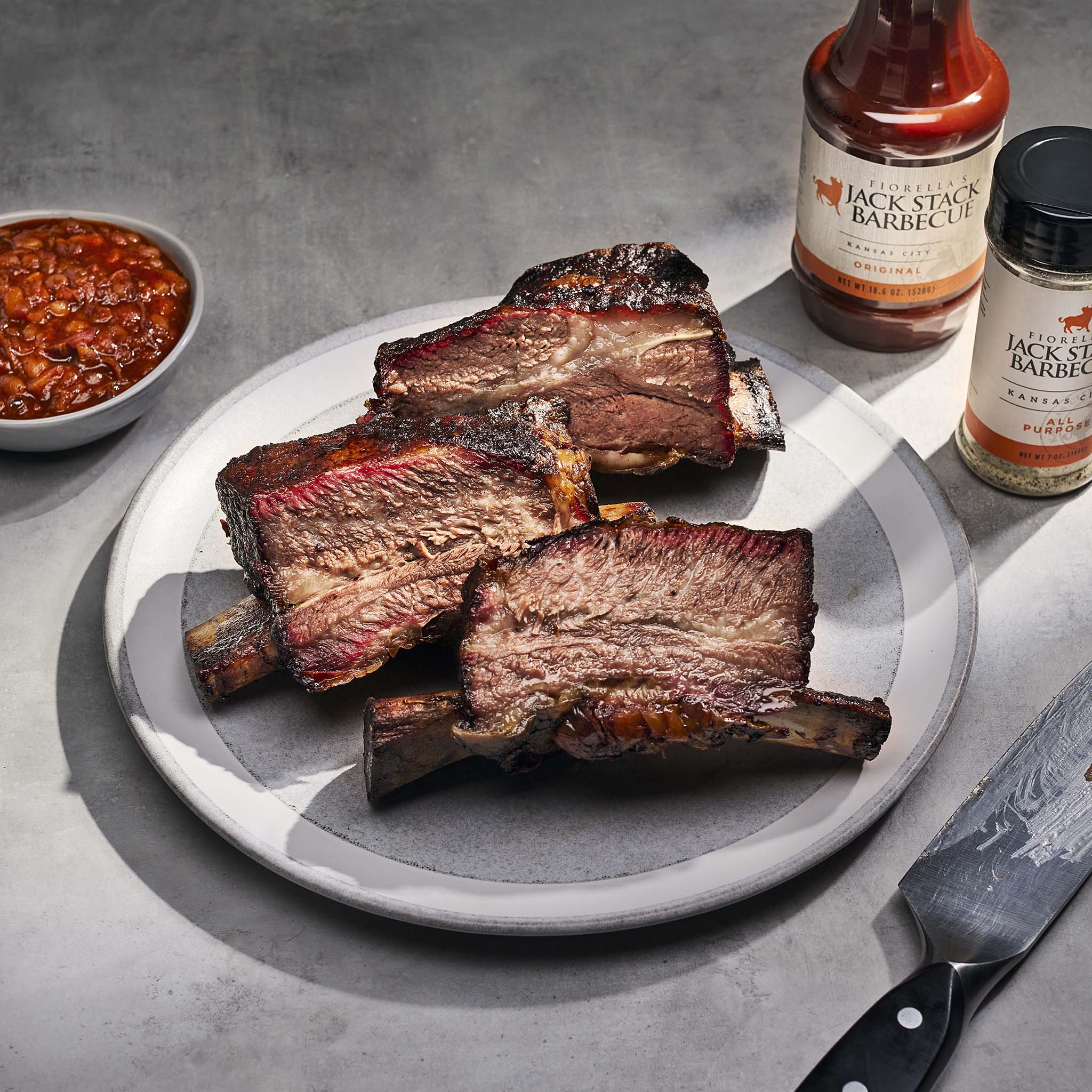 Bbq ribs on a plate with Jack Stack Barbecue products on a gray surface