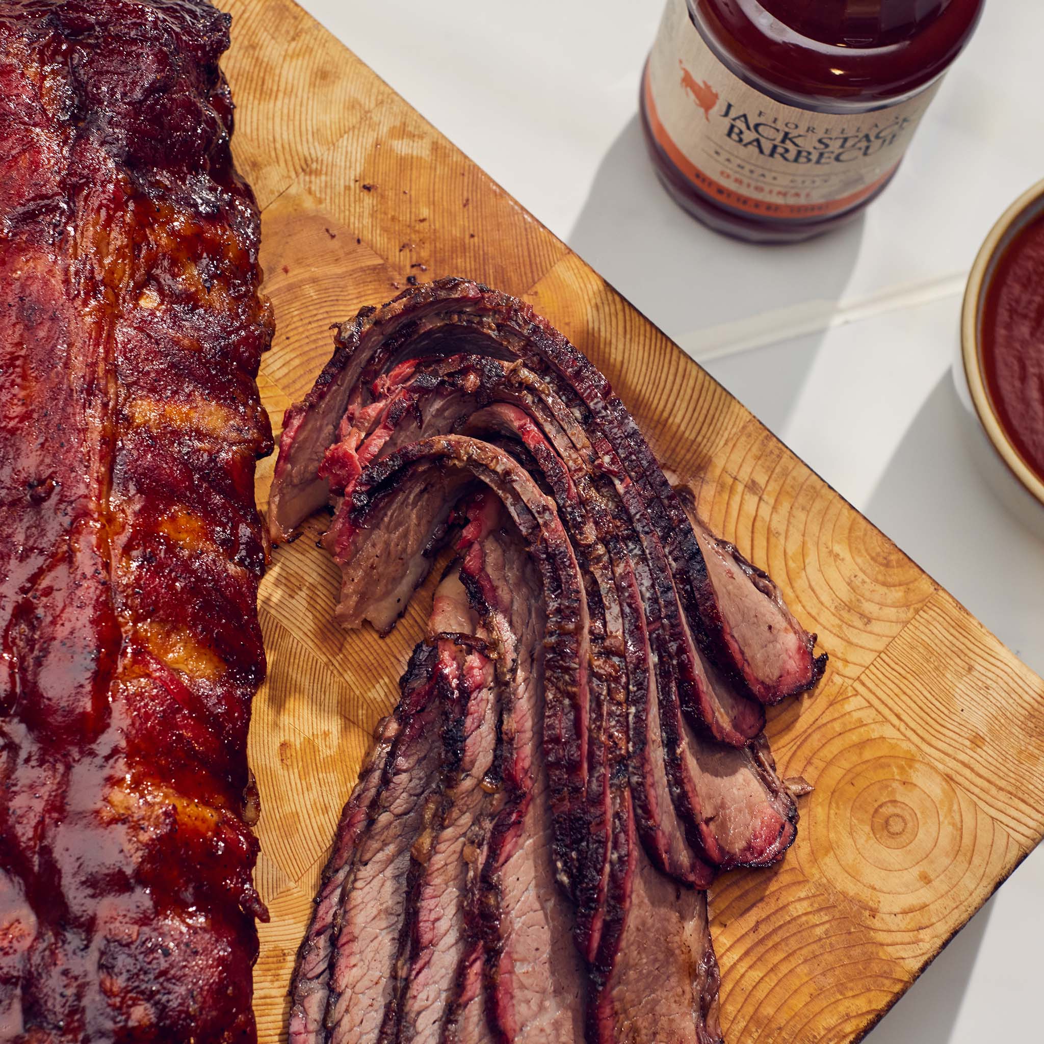 Sliced ribs on a wooden cutting board with a jar of barbecue sauce in the background.