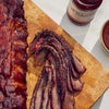 Sliced ribs on a wooden cutting board with a jar of barbecue sauce in the background.