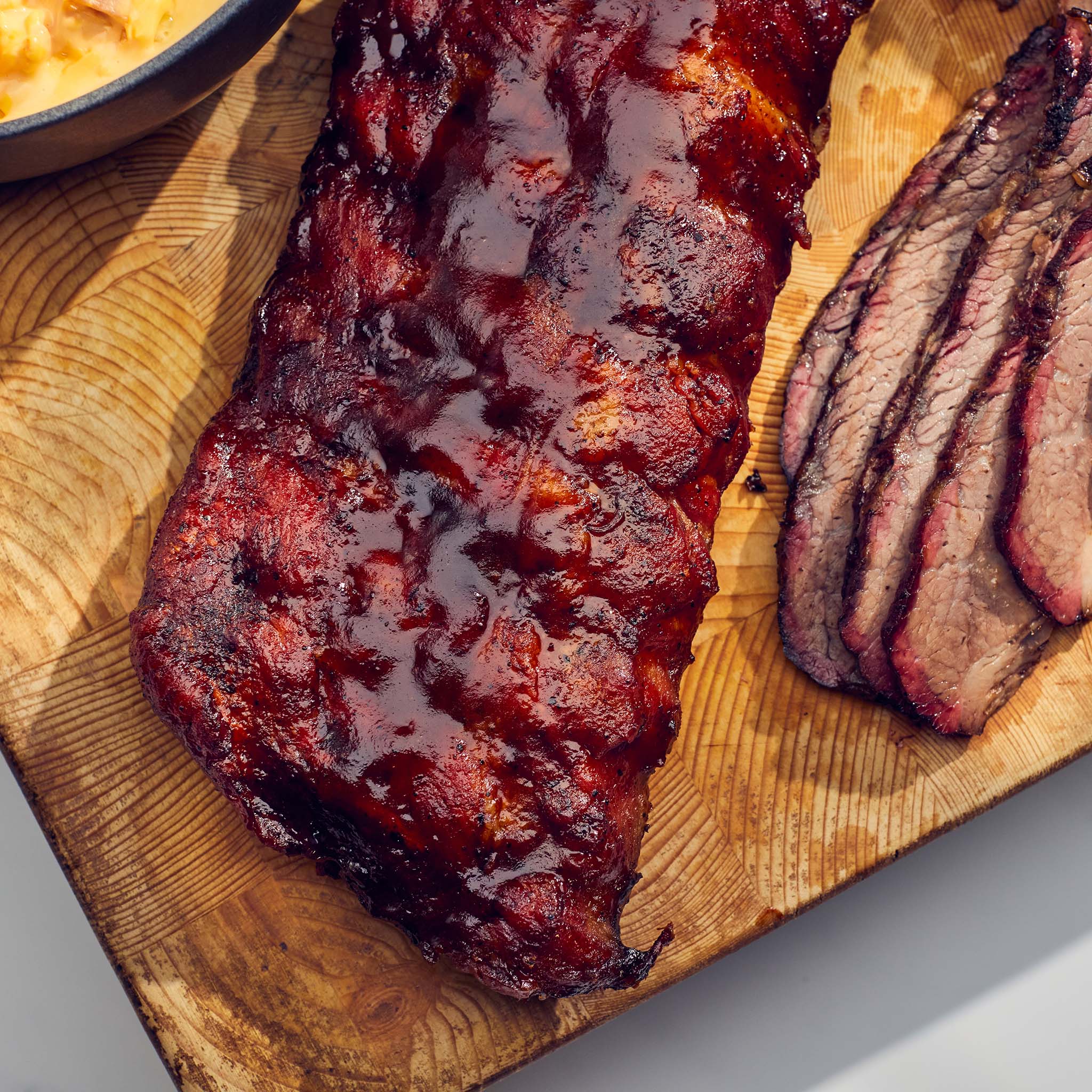 BBQ ribs on a wooden cutting board with a side of sliced meat.