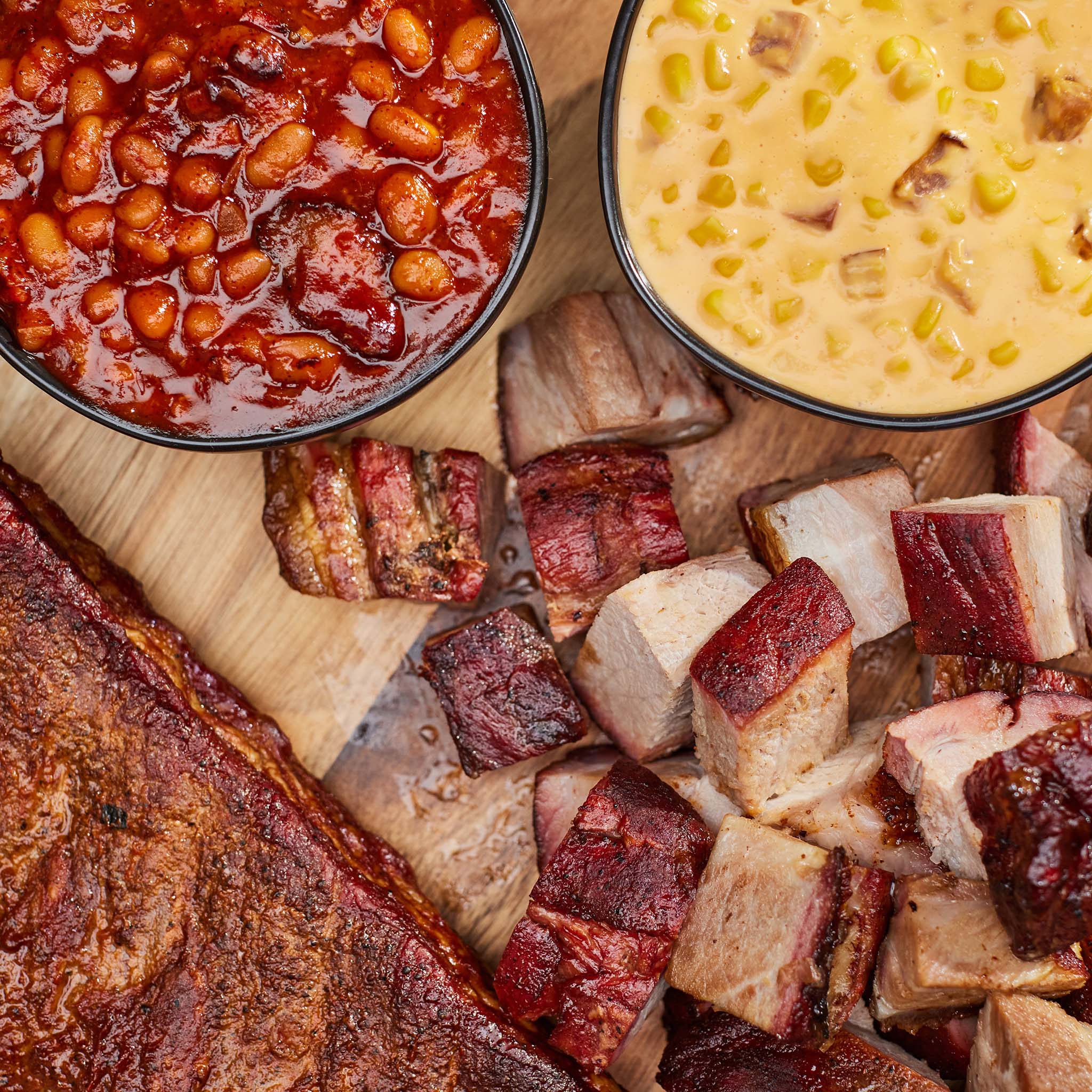 Platter with barbecue ribs, baked beans, and mac and cheese on a wooden surface