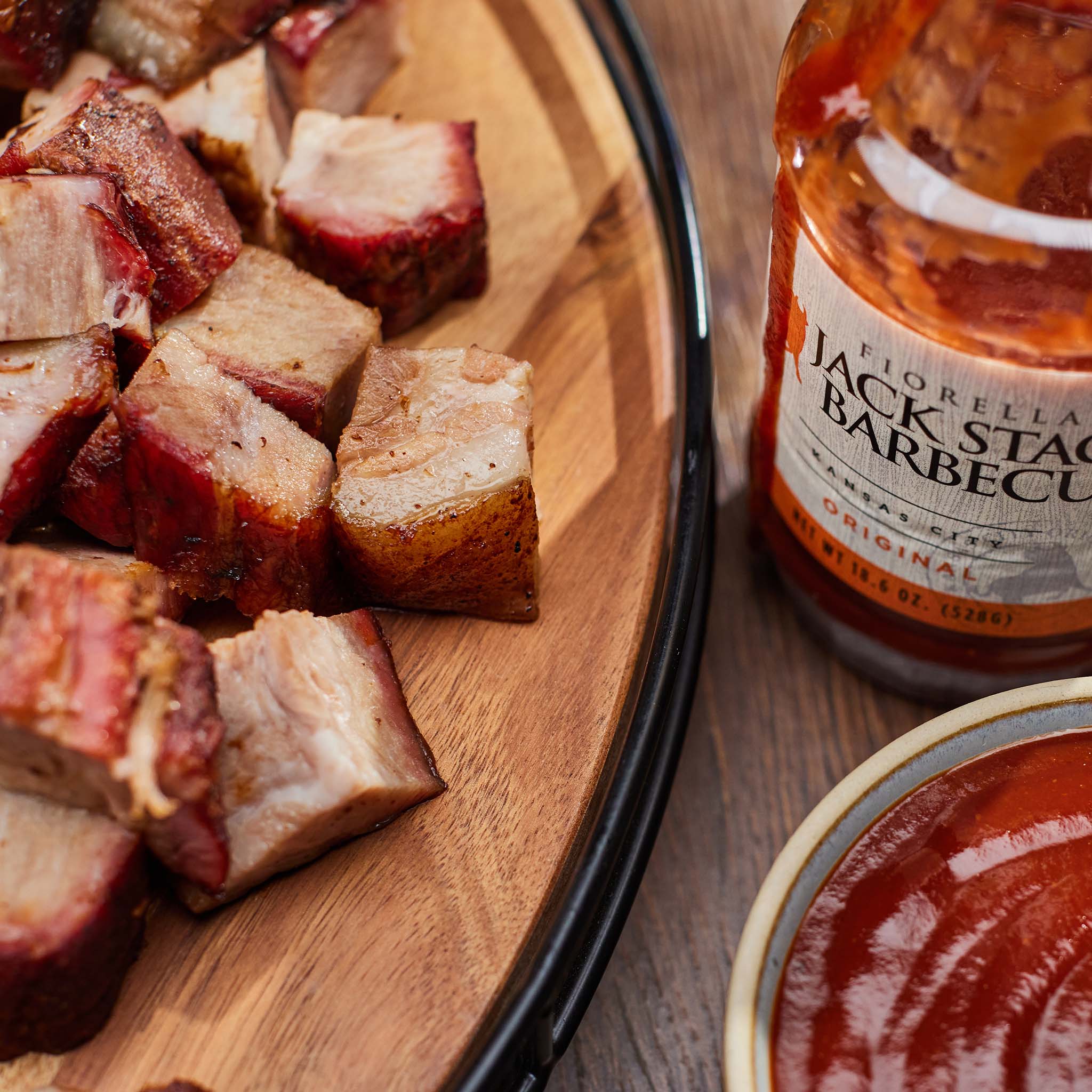 Diced smoked meat on a wooden board with a jar of Jack Stack Barbecue sauce.