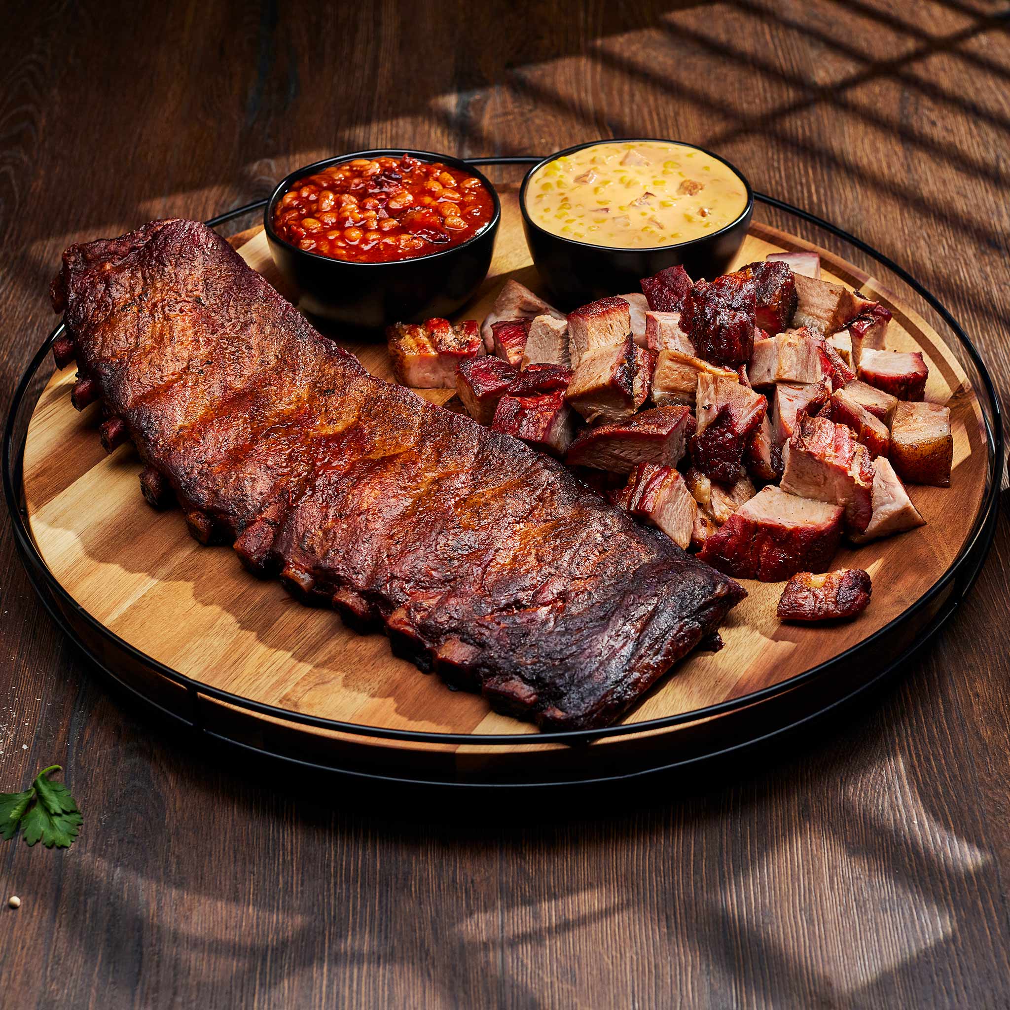 Platter of ribs and cut meats with side dishes on a wooden surface