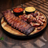Platter of ribs and cut meats with side dishes on a wooden surface