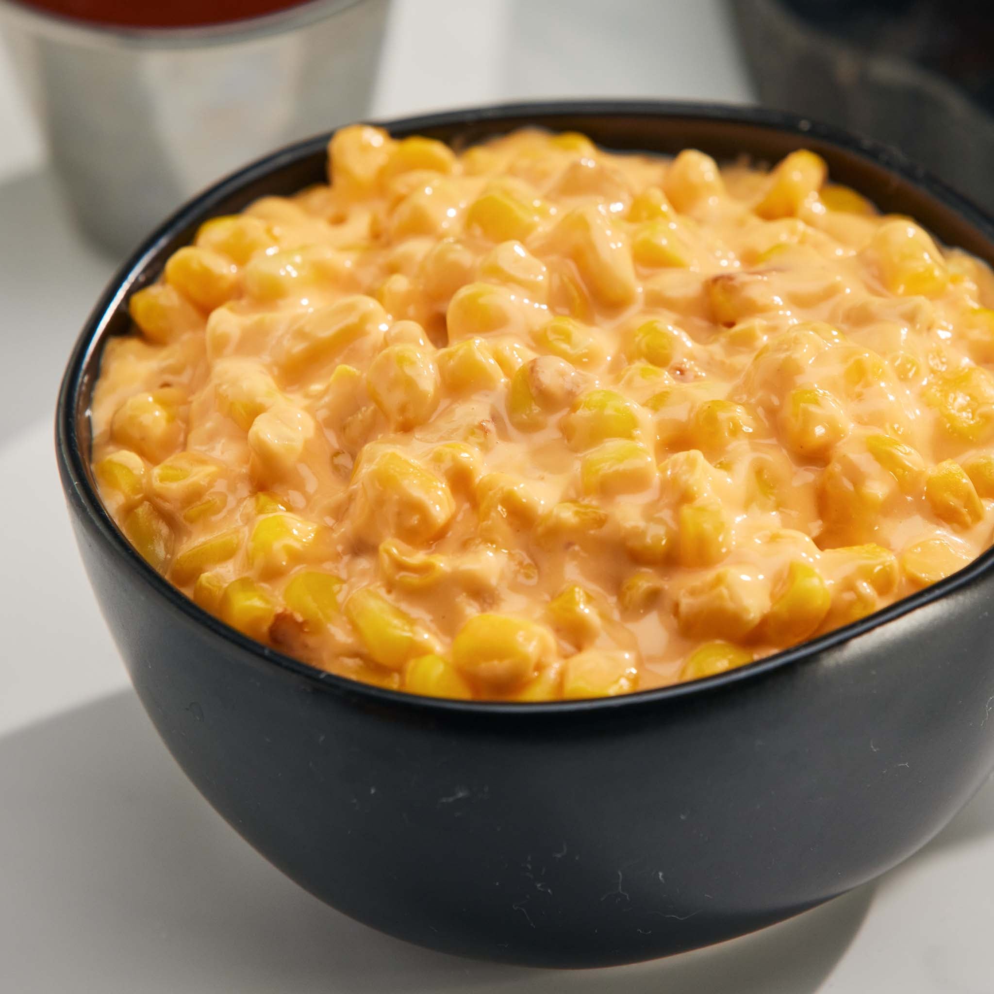 Black bowl filled with cheesy corn on a white surface