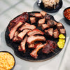 Platter of barbecue ribs and chunks on a dark surface with sides of macaroni and cheese and beans.