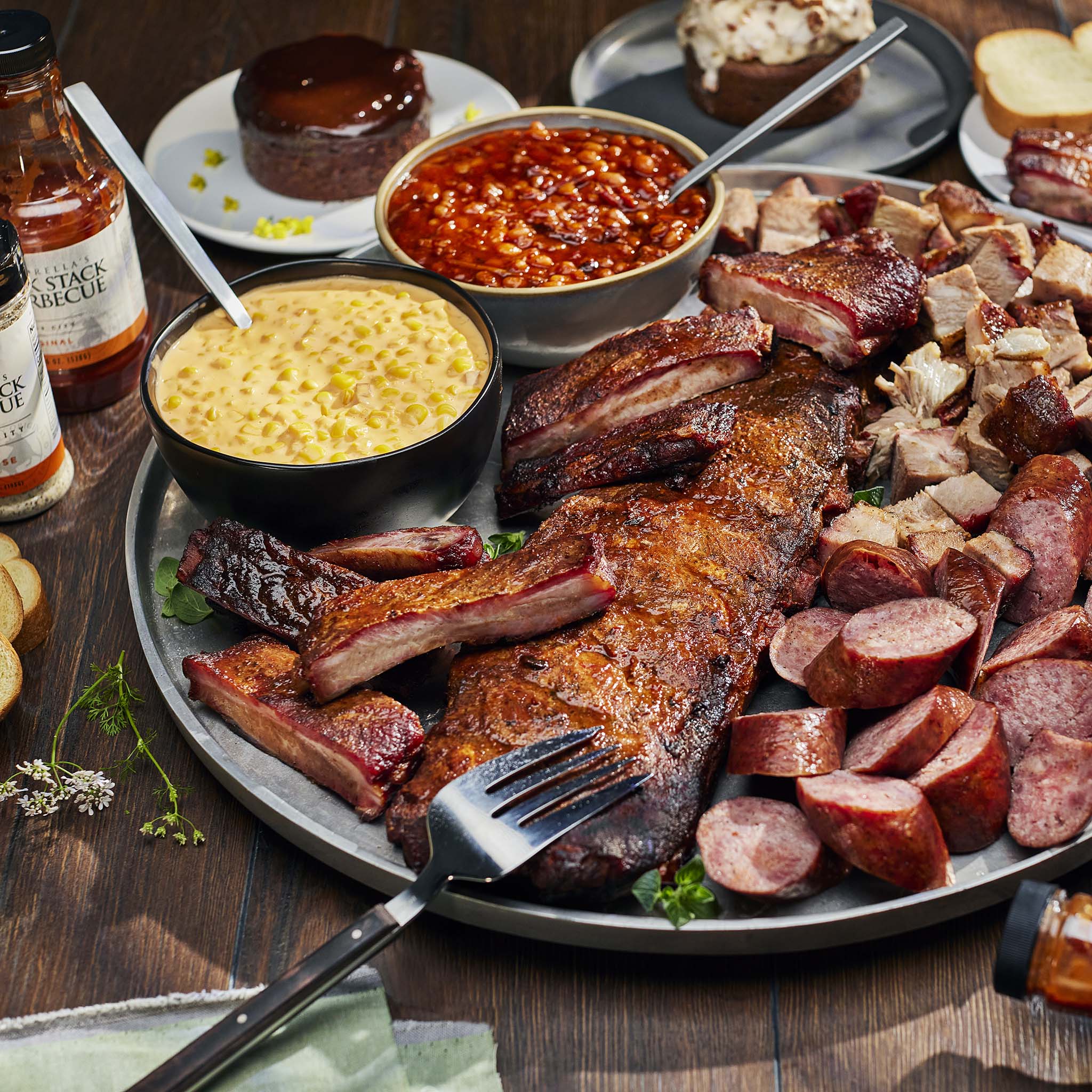 Platter of barbecue meats including ribs, sausages, and macaroni and cheese on a wooden table.