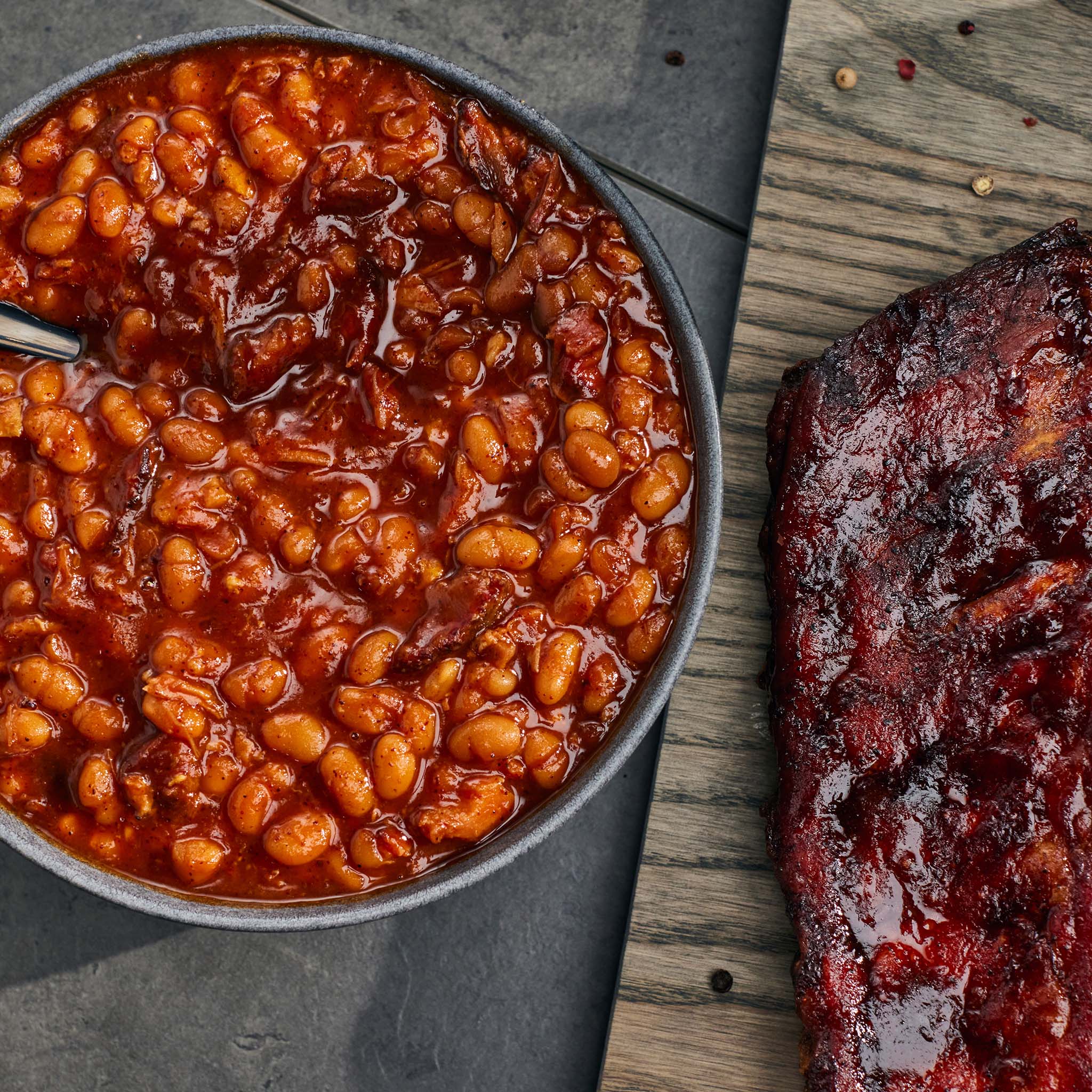 Baked beans in a bowl next to a rib on a wooden surface