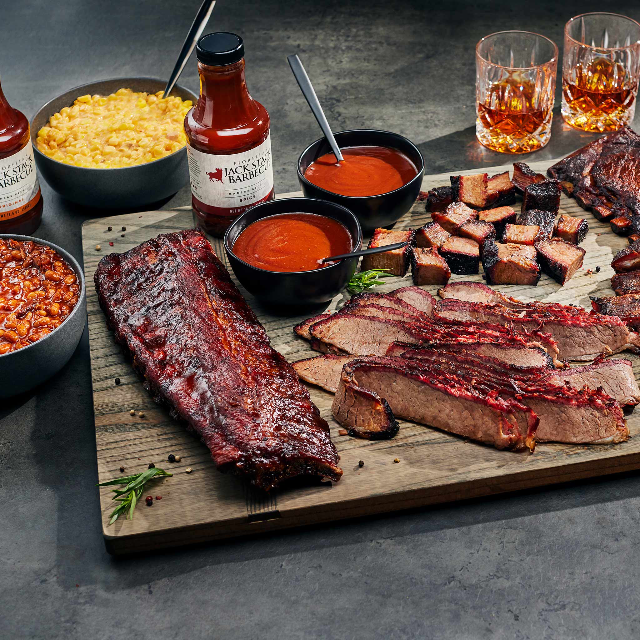 Platter of barbecue meats with sides and sauces on a wooden board.