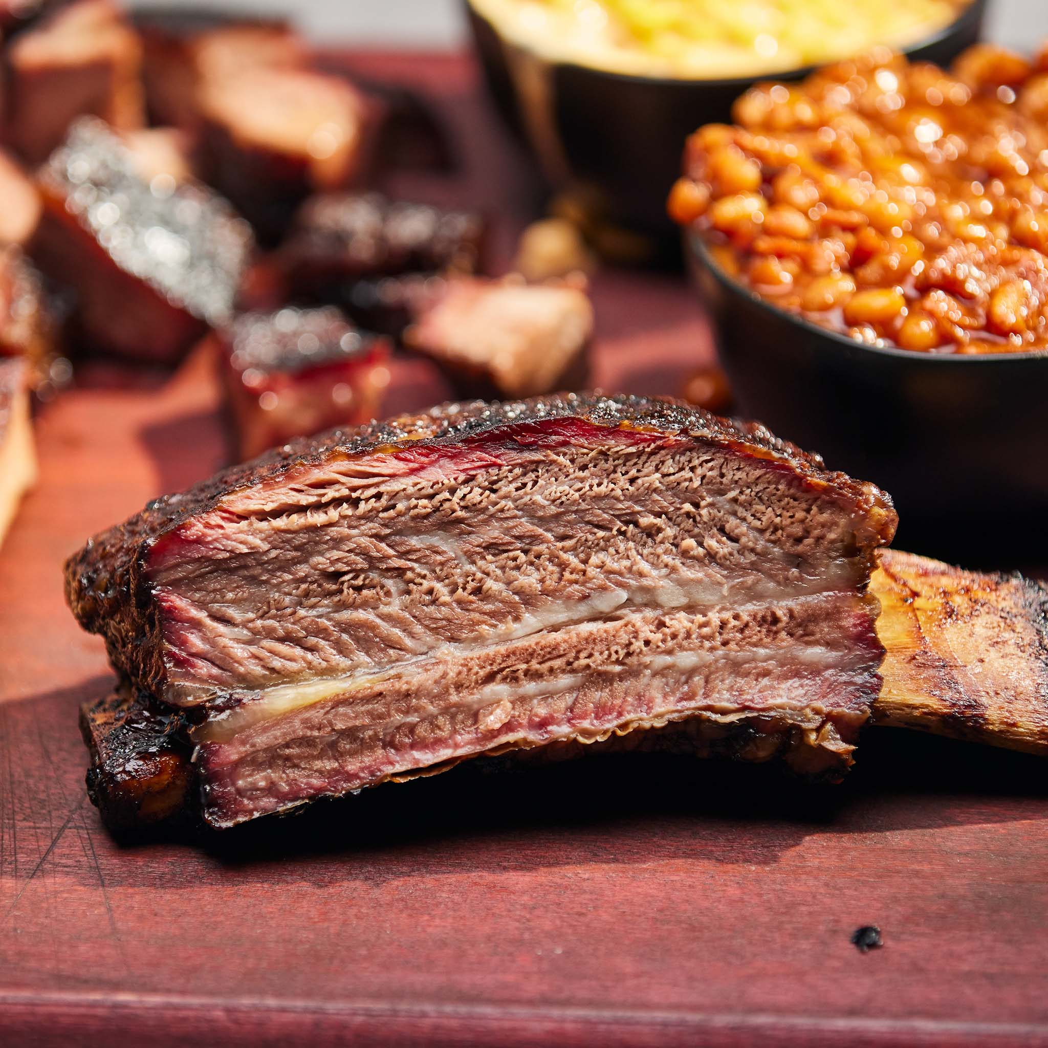 Close-up of a ribeye steak on a wooden cutting board with sides in the background