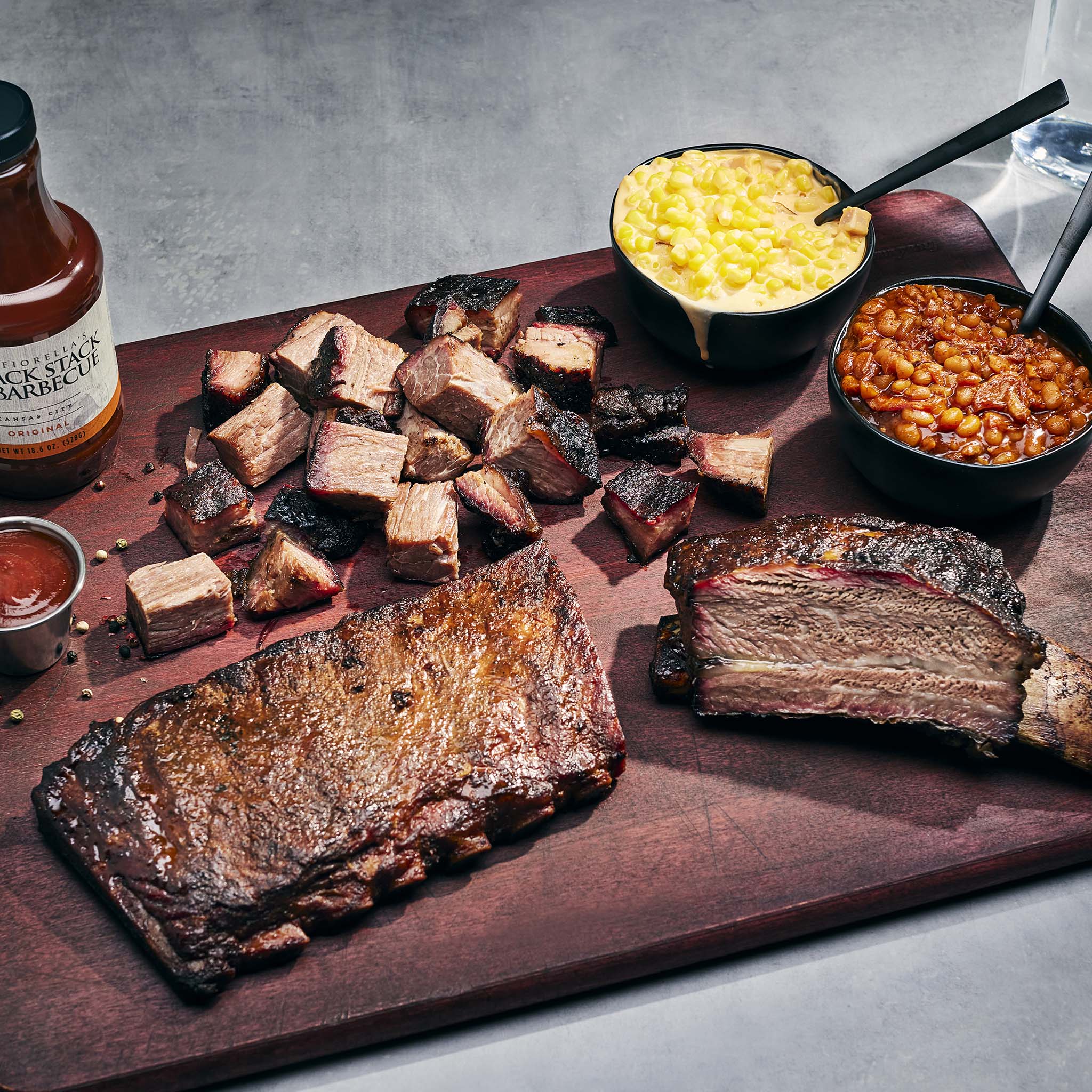 Assorted barbecue meats on a wooden board with sides of mac and cheese and baked beans.