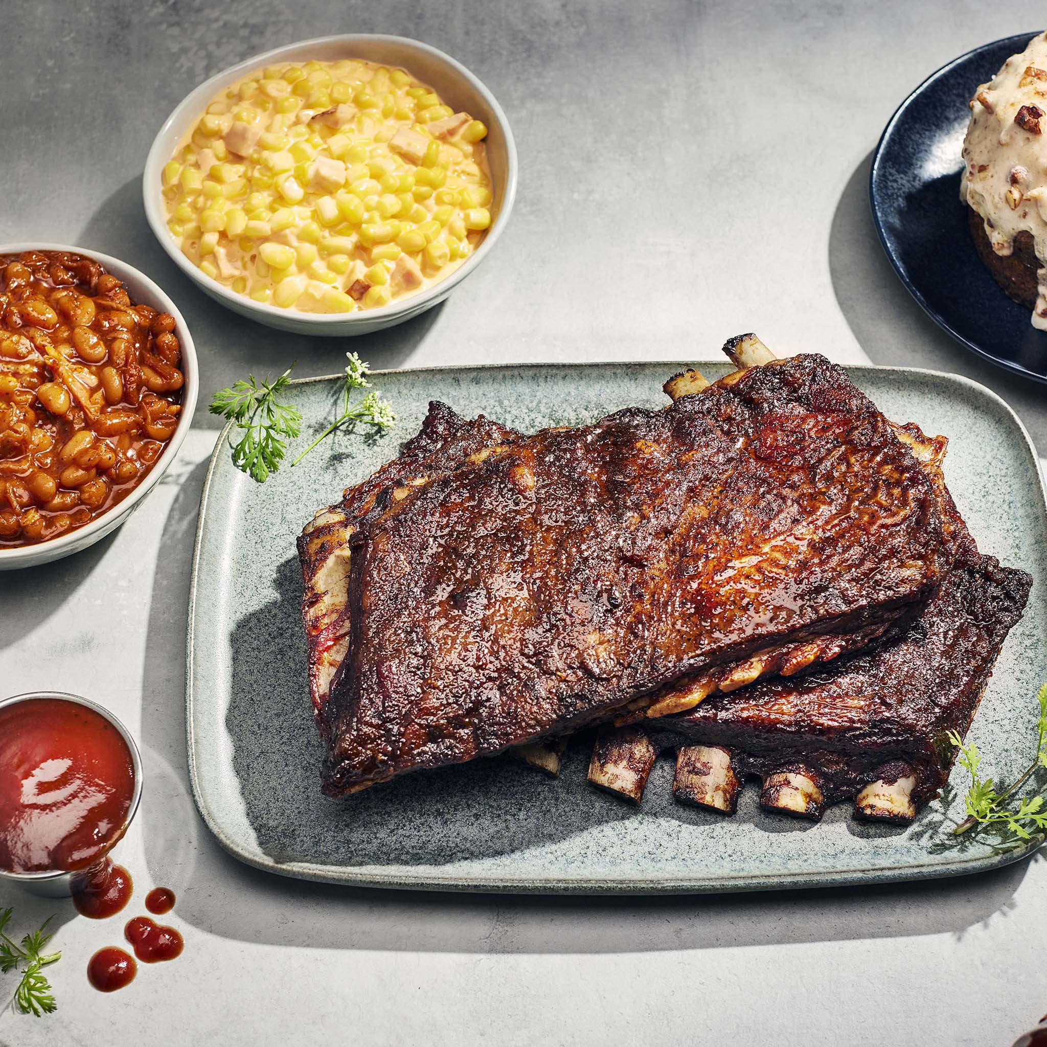 Plated ribs with sides of baked beans and corn on a gray surface