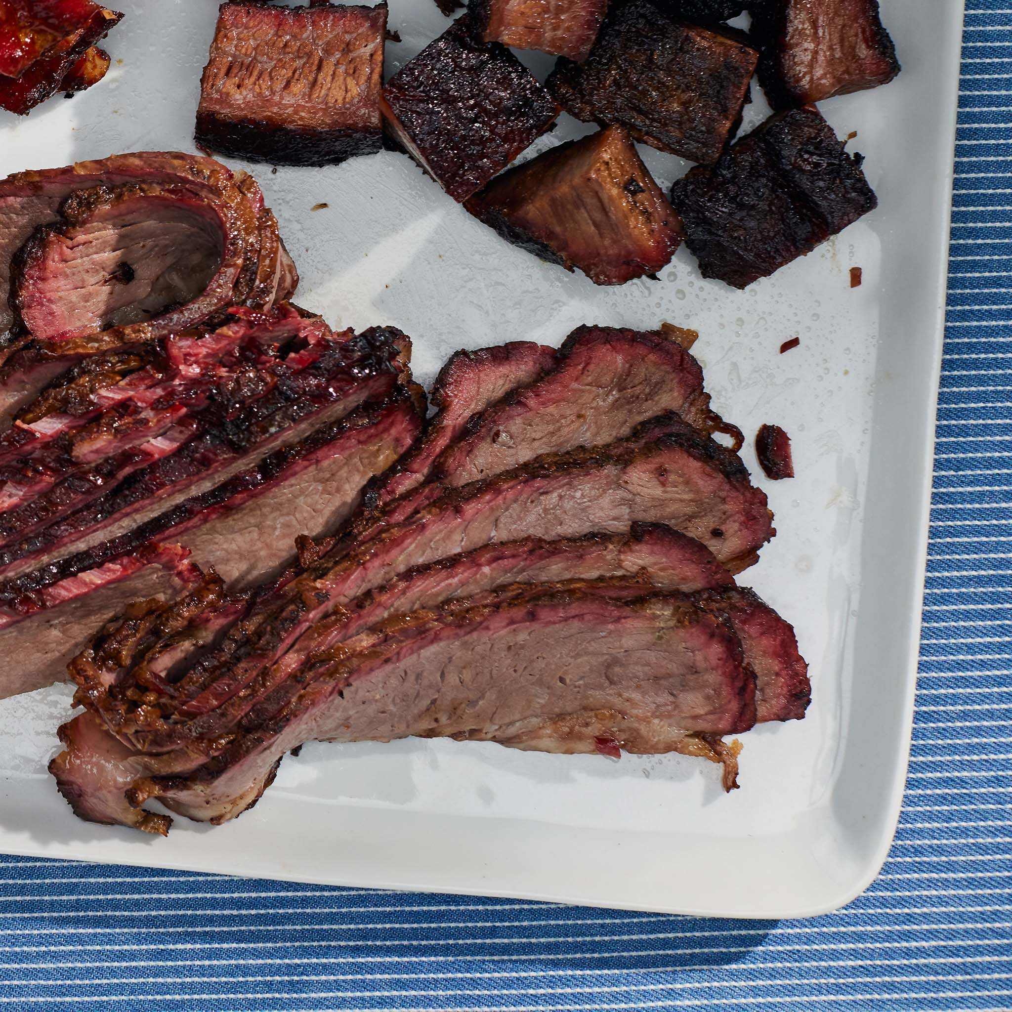Sliced beef brisket on a white plate with a blue striped tablecloth underneath